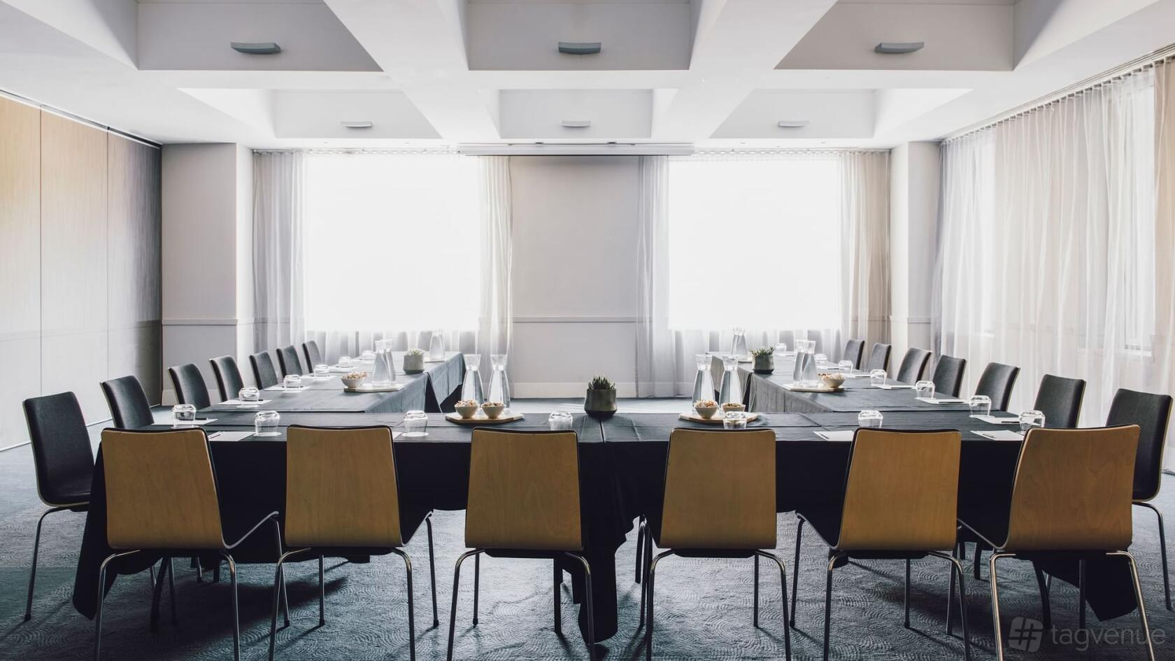 A hotel meeting room with U-shaped tables, black linens, wooden chairs, and large windows at The Como Melbourne.