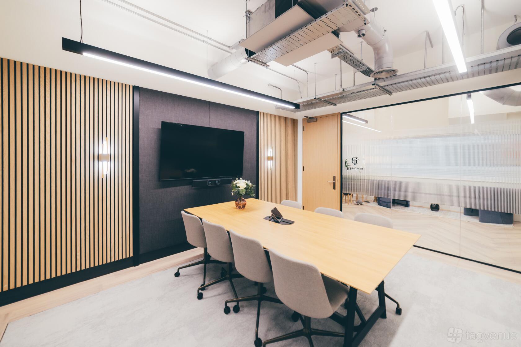 A meeting centre with a long wooden table, grey chairs, wall-mounted TV, and slatted wood paneling at Orega The Tootal Buildings.