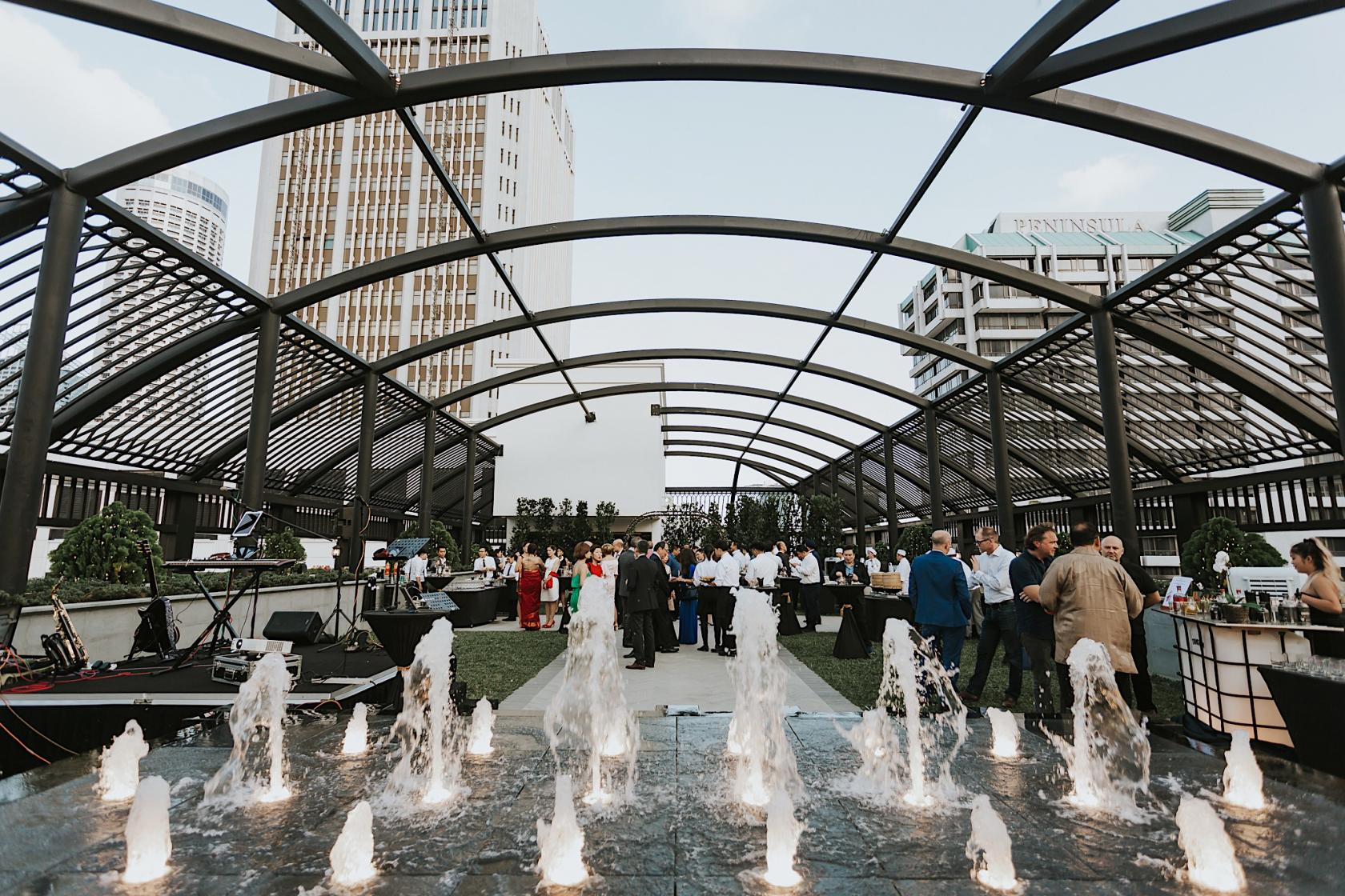 A hotel rooftop with an open-air pergola, water fountains, and guests mingling at Grand Park City Hall.
