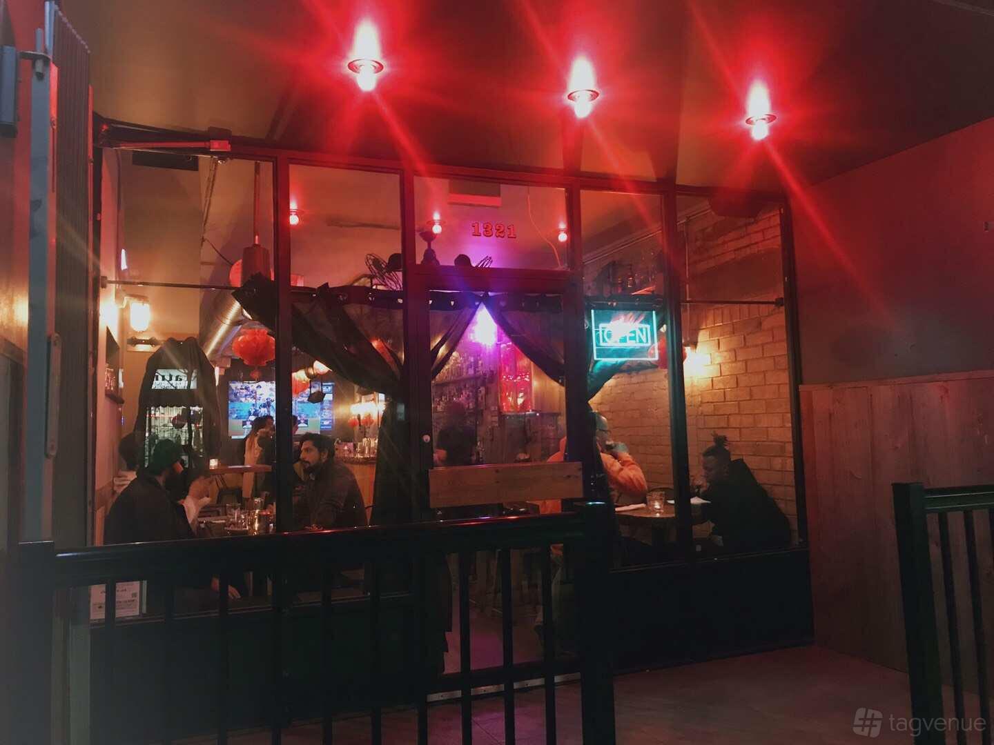A cozy pub with red lighting, brick walls, and neon signs at The Opium Bar.
