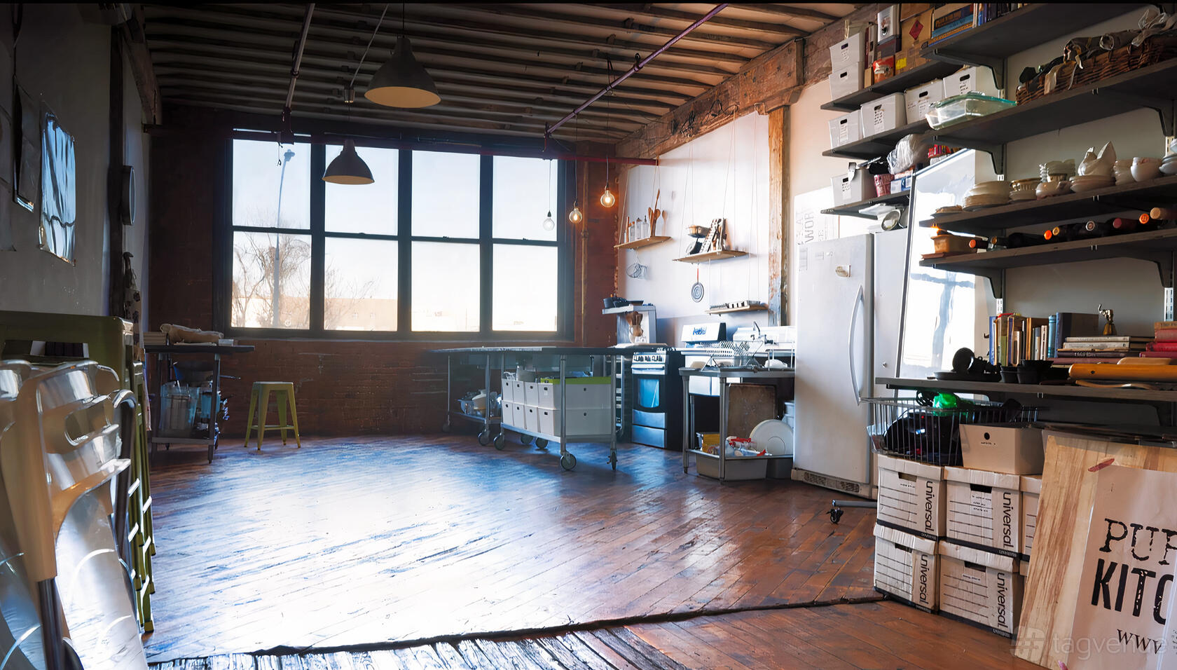 A loft with large industrial windows, exposed beams, and an open kitchen with stainless appliances at Purple Kale.