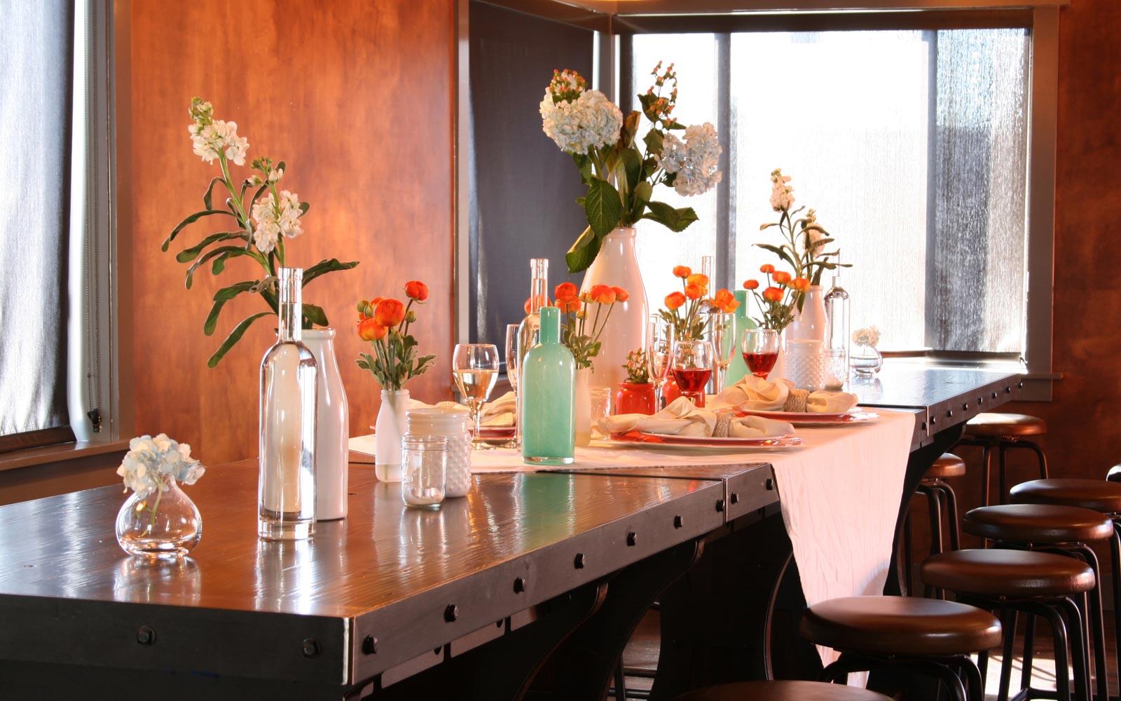 An event venue with a long wooden table, black stools, and floral centerpieces at Marigold Private Event Space.