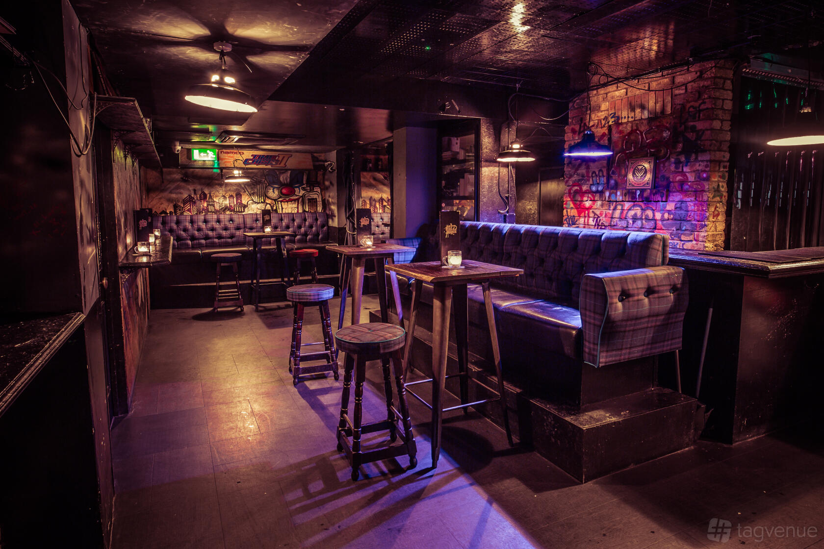 A cocktail bar with tufted banquette seating, high tables, and exposed brick walls at The Cocktail Club Oxford Circus.