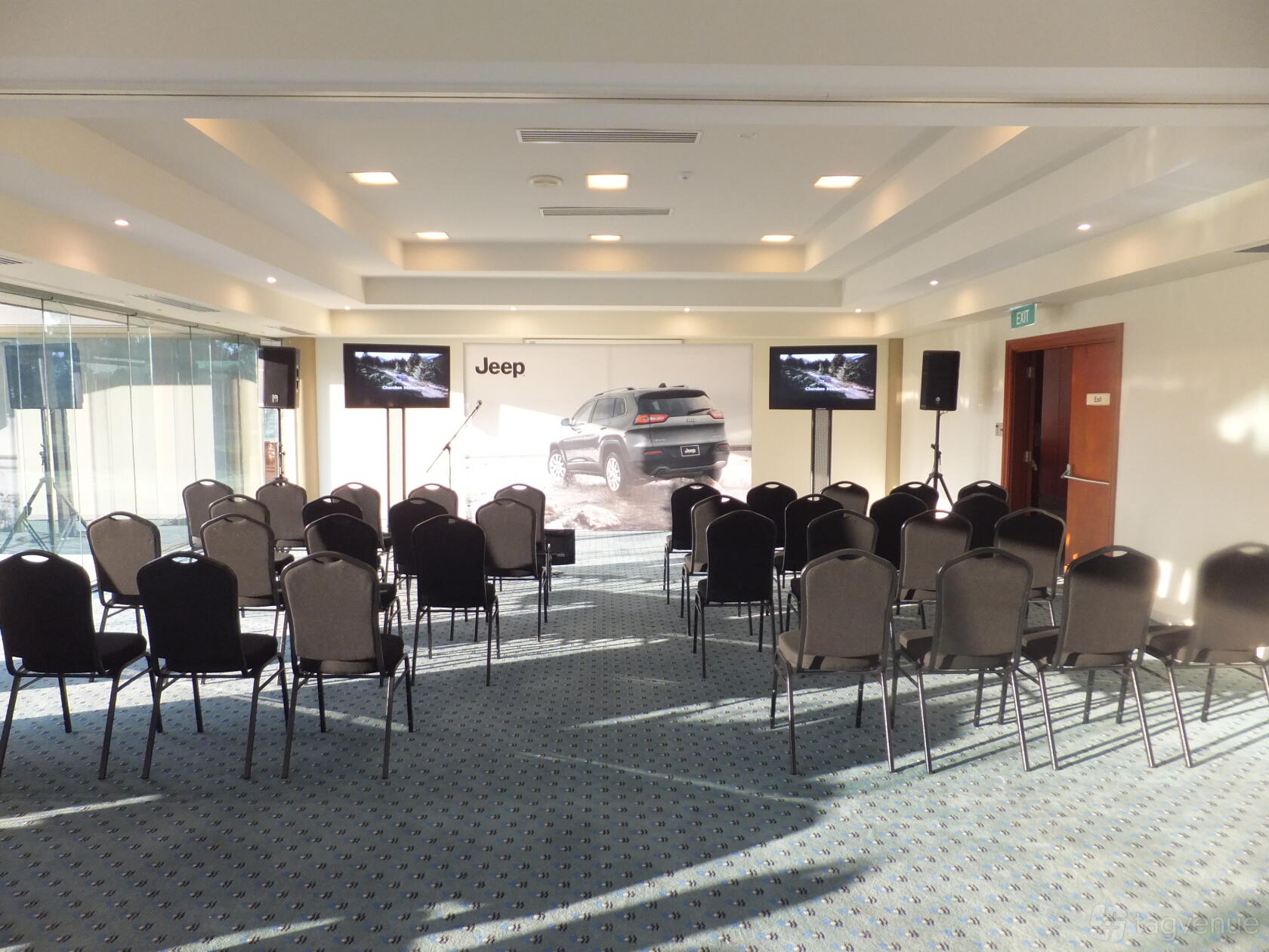 A meeting room with rows of black chairs, carpeted floors, and two display screens at Riverside Oaks Resort.