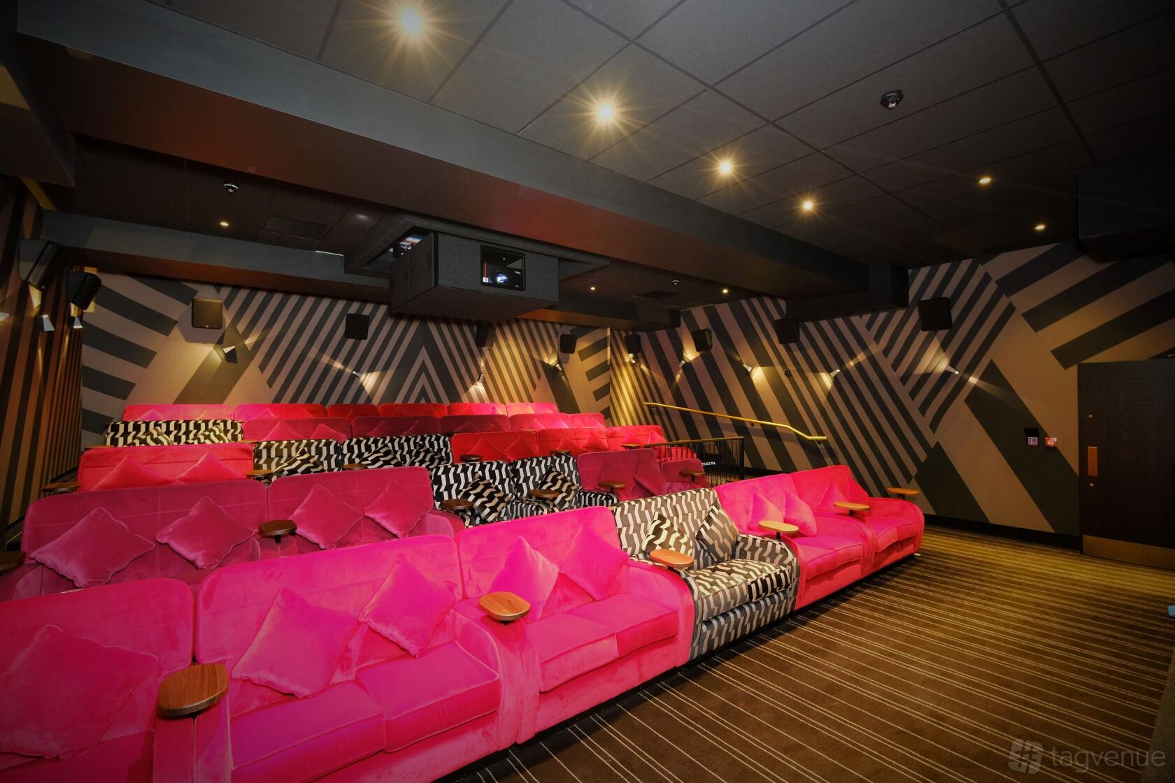 A cinema screening room with tiered pink and zebra-print sofas, wall-mounted speakers, and striped walls at Everyman Altrincham.
