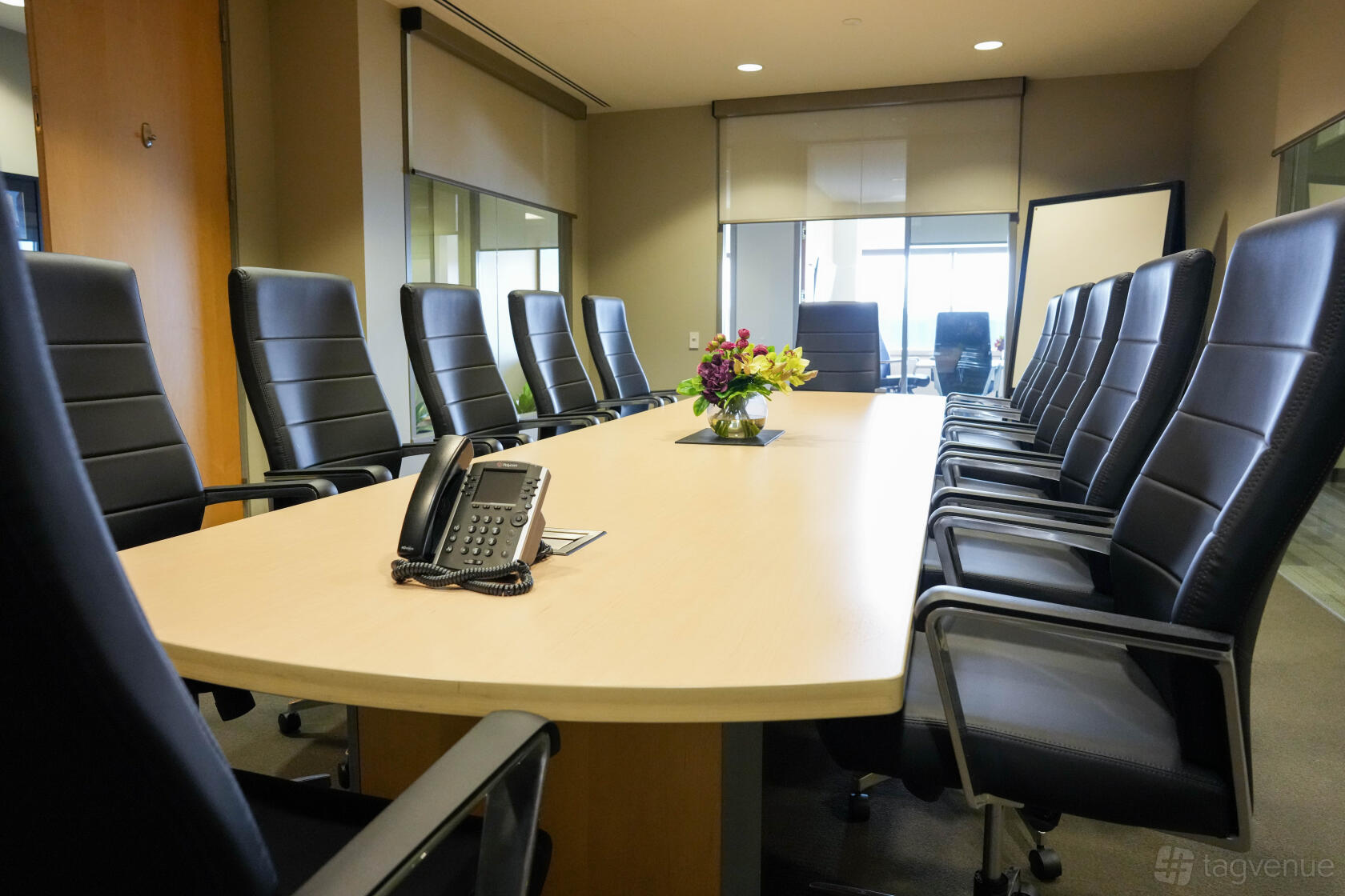 A meeting room with a long conference table, black leather chairs, and a floral centerpiece at Intelligent Office - First Canadian Place.