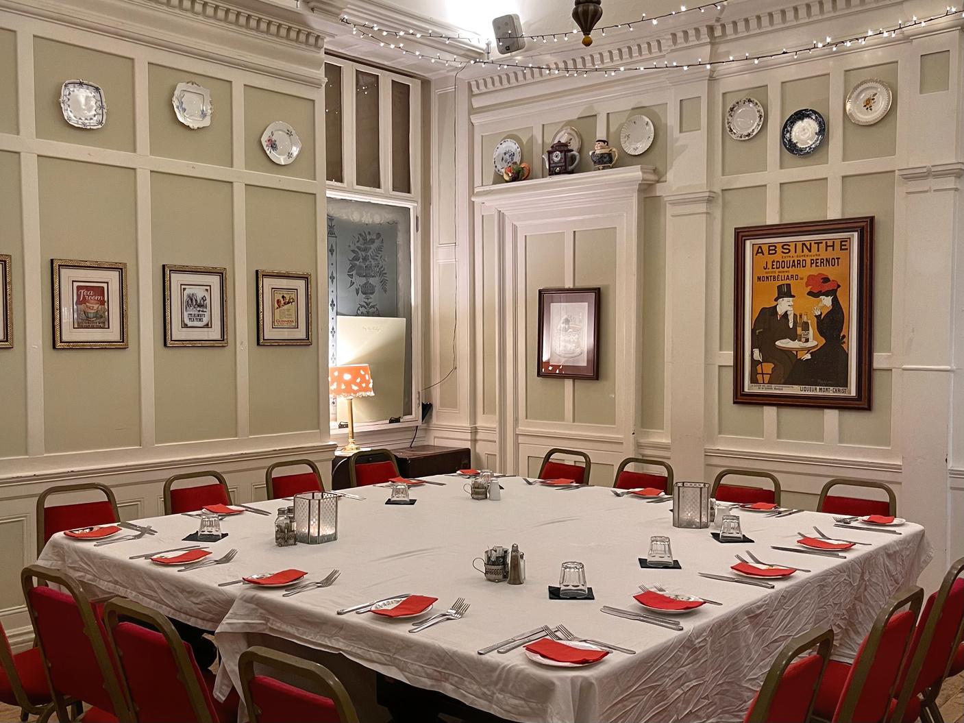 A dining room with red chairs, a square table with white linens, framed prints, and decorative plates at The Butterfly and The Pig.