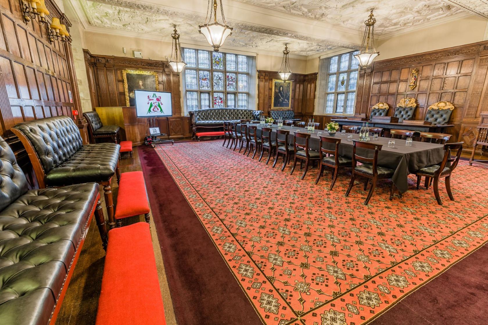 An event space in a hall with wood-paneled walls, ornate ceiling, and long tables with black linens at Ironmongers' Hall.