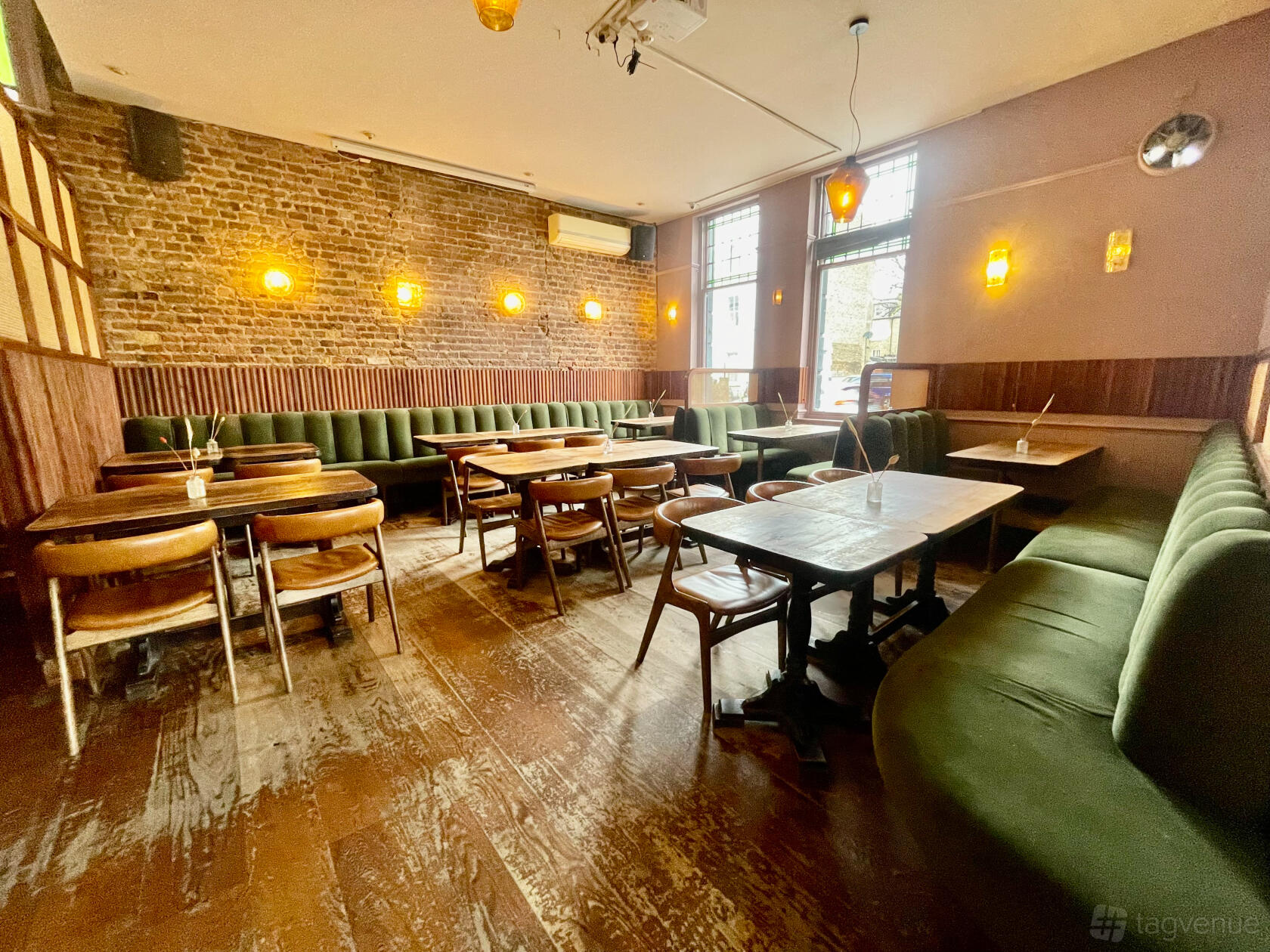 A bar with exposed brick walls, green velvet banquette seating, and wooden tables at The Lauriston.