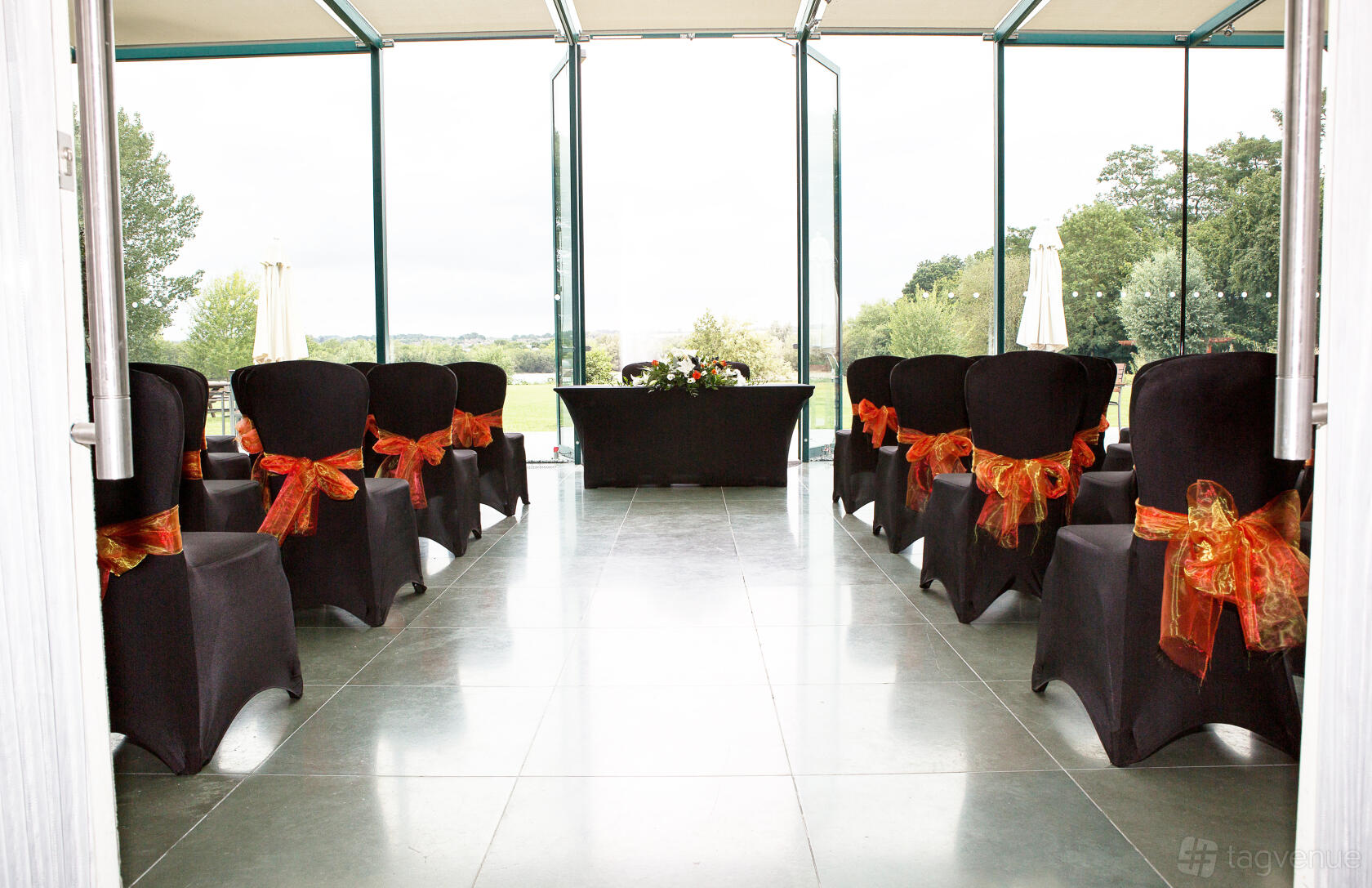 An event space with floor-to-ceiling windows, black chair covers with orange ribbons, and outdoor views at Crowne Plaza Marlow.