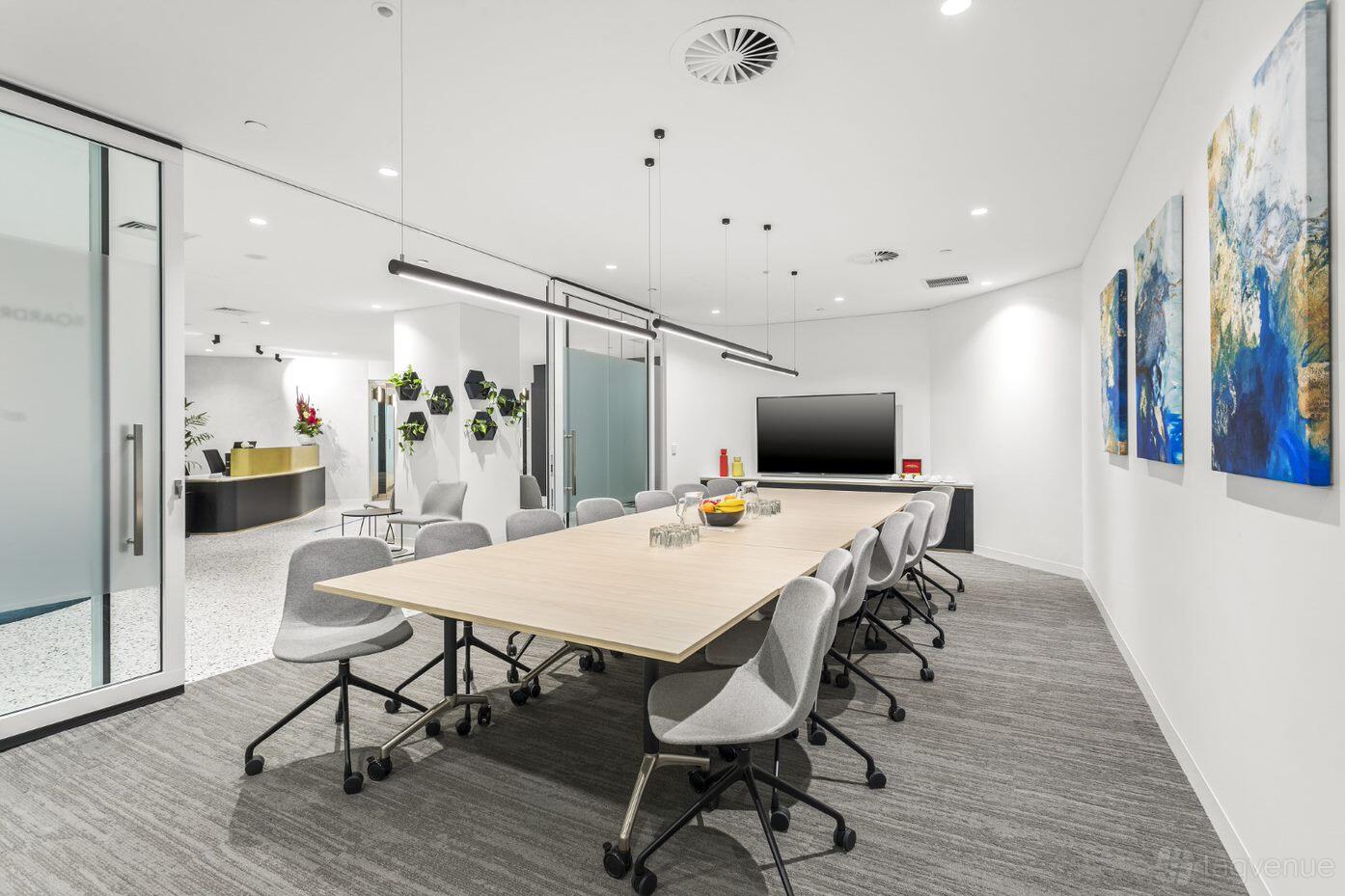 A boardroom with a long conference table, gray chairs, wall art, and a TV screen at Opus Workspaces.
