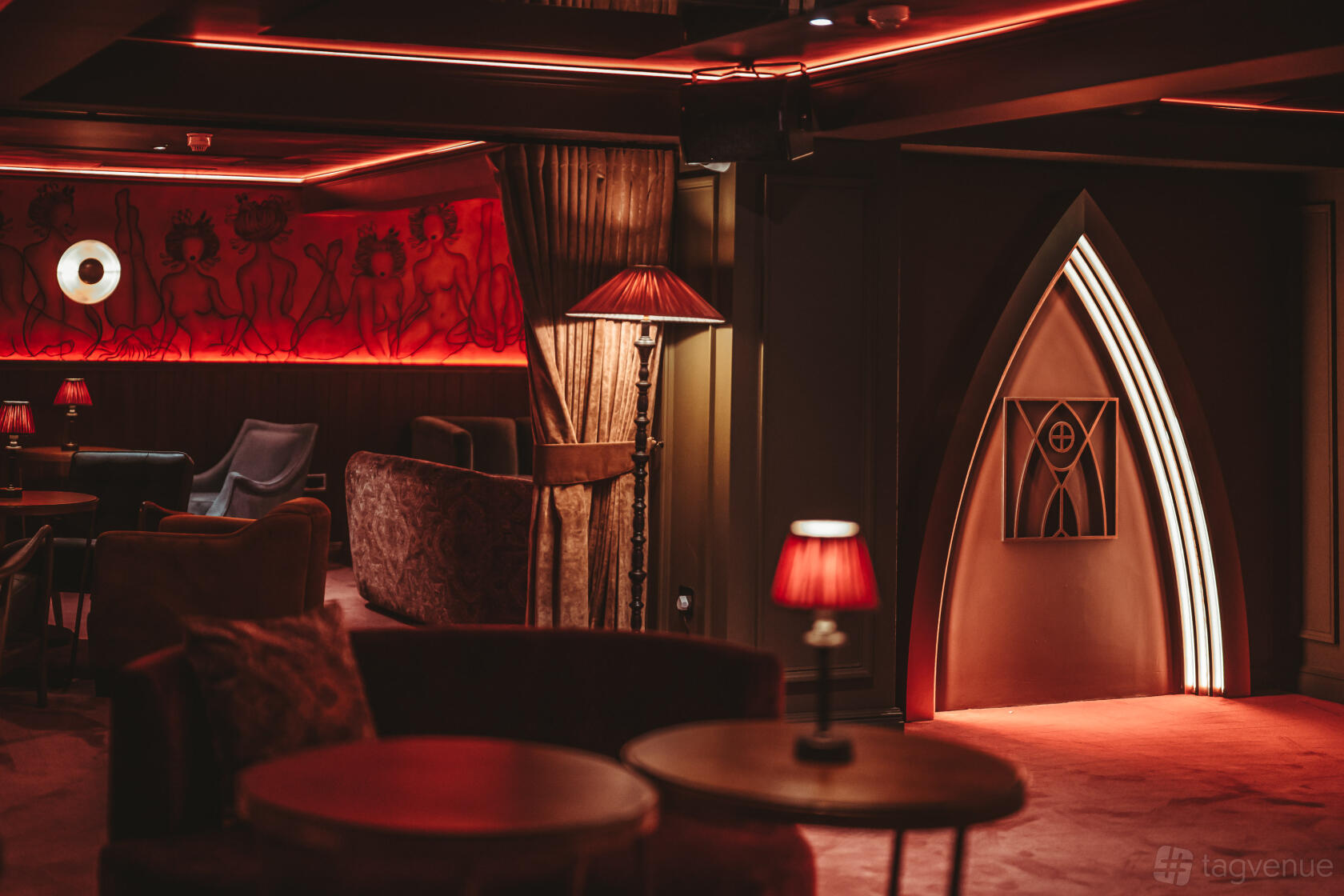 A nightclub lounge with red velvet seating, ambient lighting, and mural artwork at Tabu London.