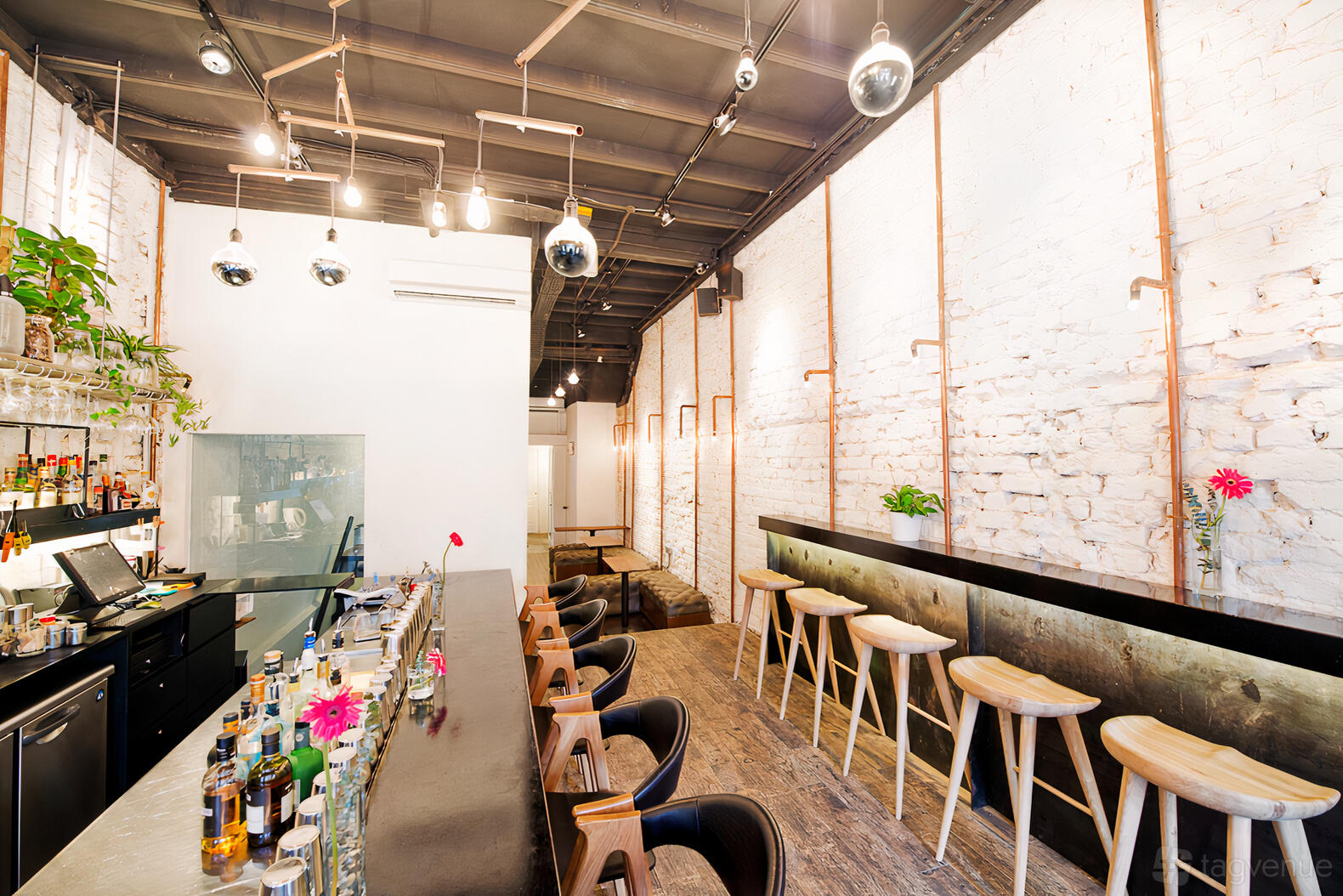 A restaurant terrace with a long bar, exposed white brick walls, high stools, and hanging pendant lights at Maison Ikkoku.