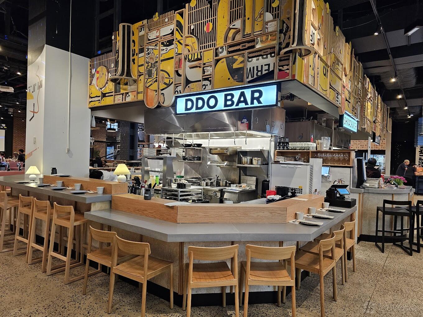An event space in a restaurant with a large open kitchen, bar seating, and illuminated DDO BAR signage at DdoBar.