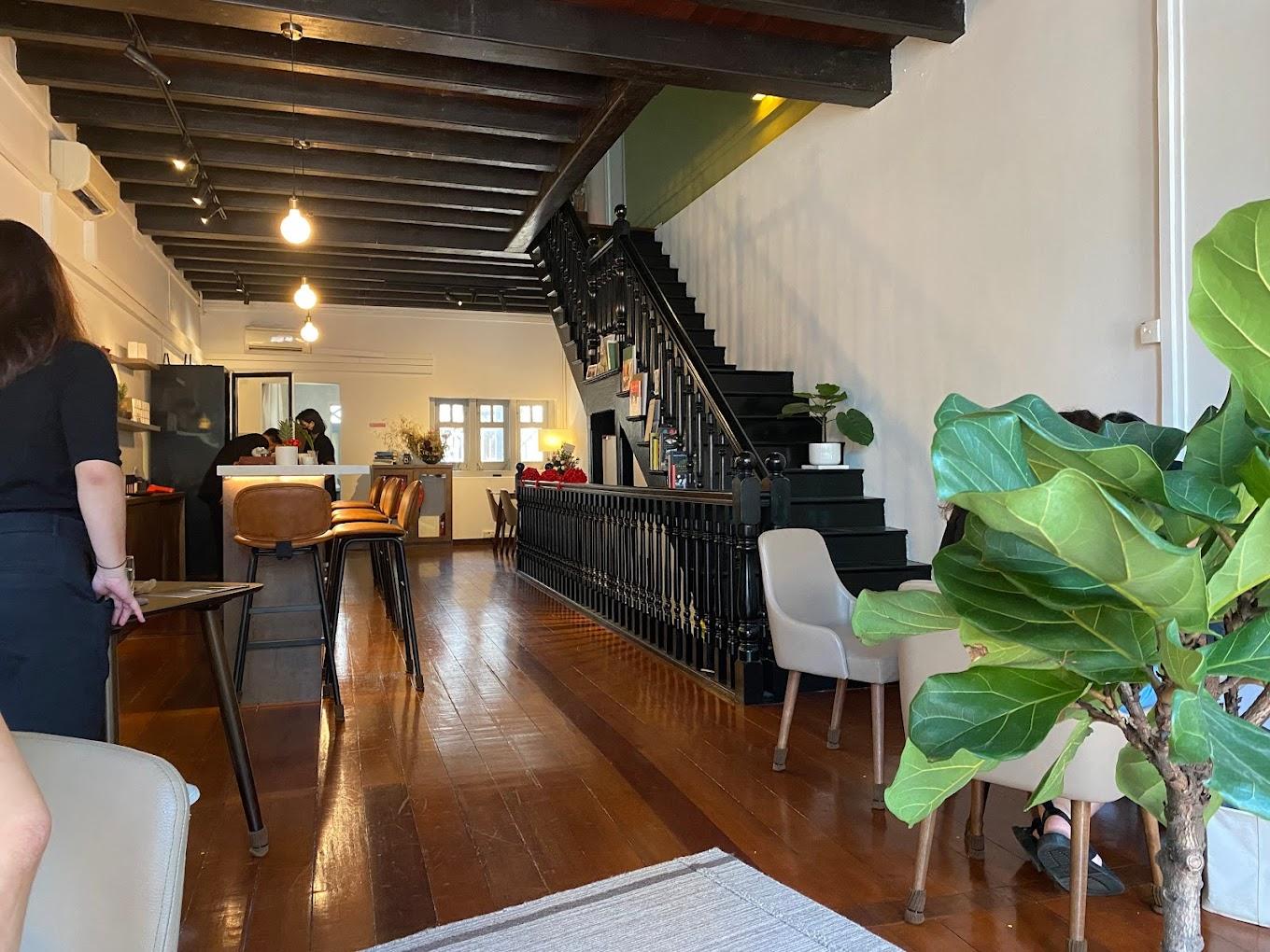 A cafe with wooden floors, black staircase, white walls, potted plants, and cushioned chairs at SILK Tea Bar.