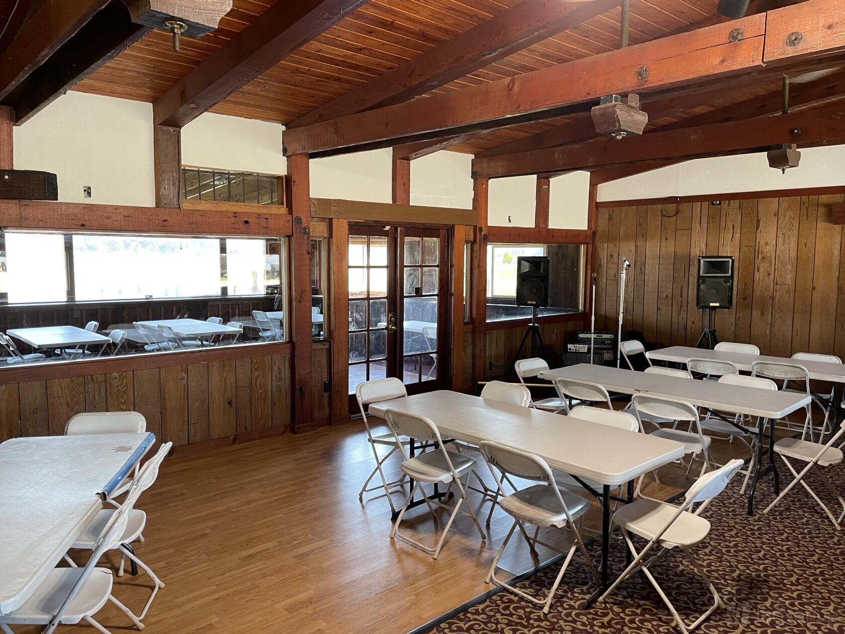 An event venue with wood-paneled walls, exposed ceiling beams, and folding tables with white chairs at The Waterfront Rodeo.