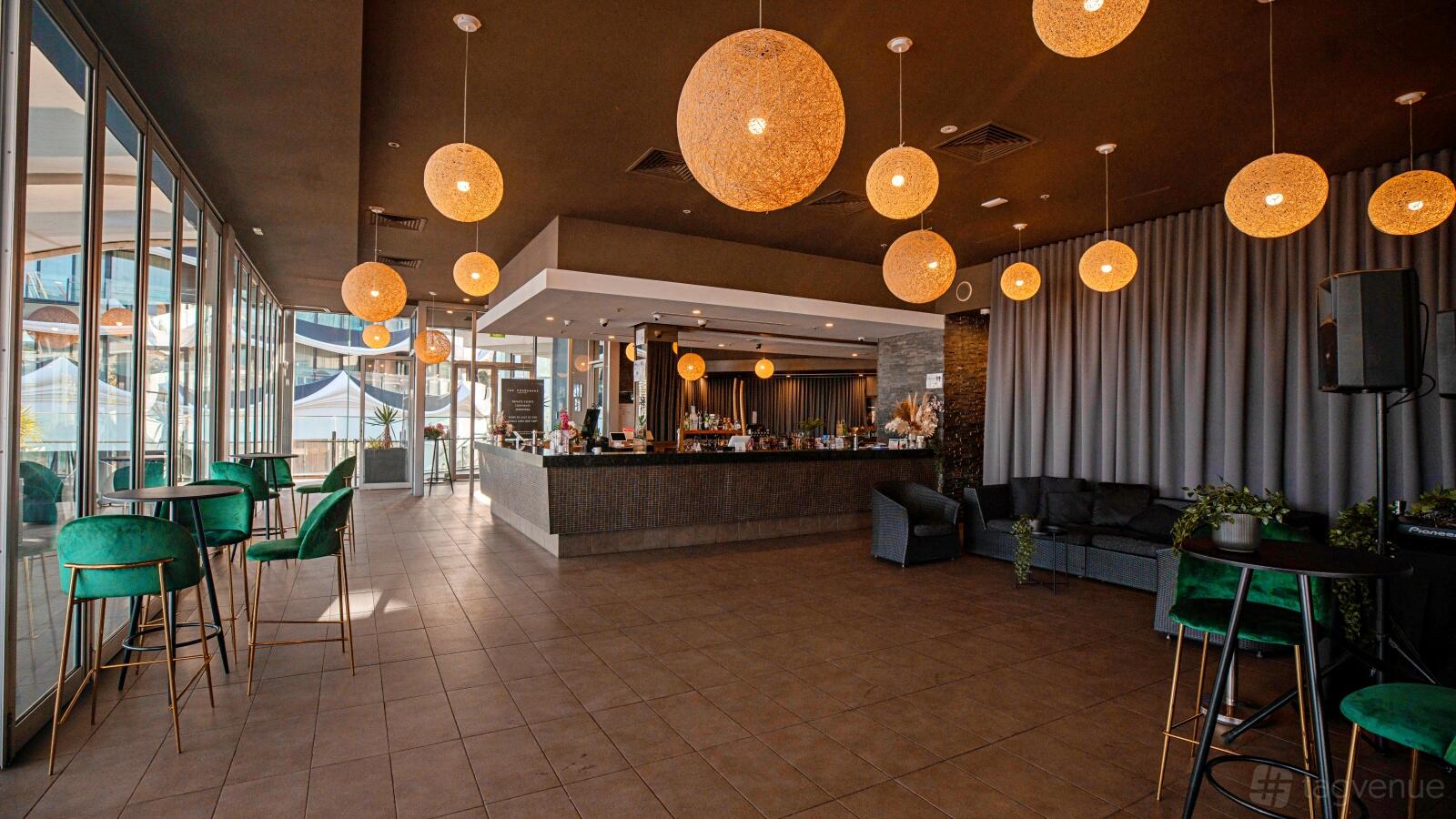A function room with globe pendant lights, tiled floors, and a central bar at The Promenade Docklands.