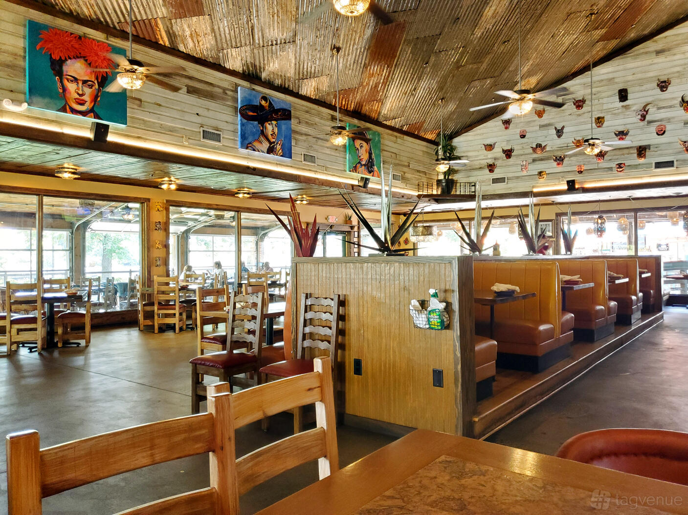 A restaurant with wooden tables, booth seating, large windows, and vibrant mural artwork at Taco Grande.