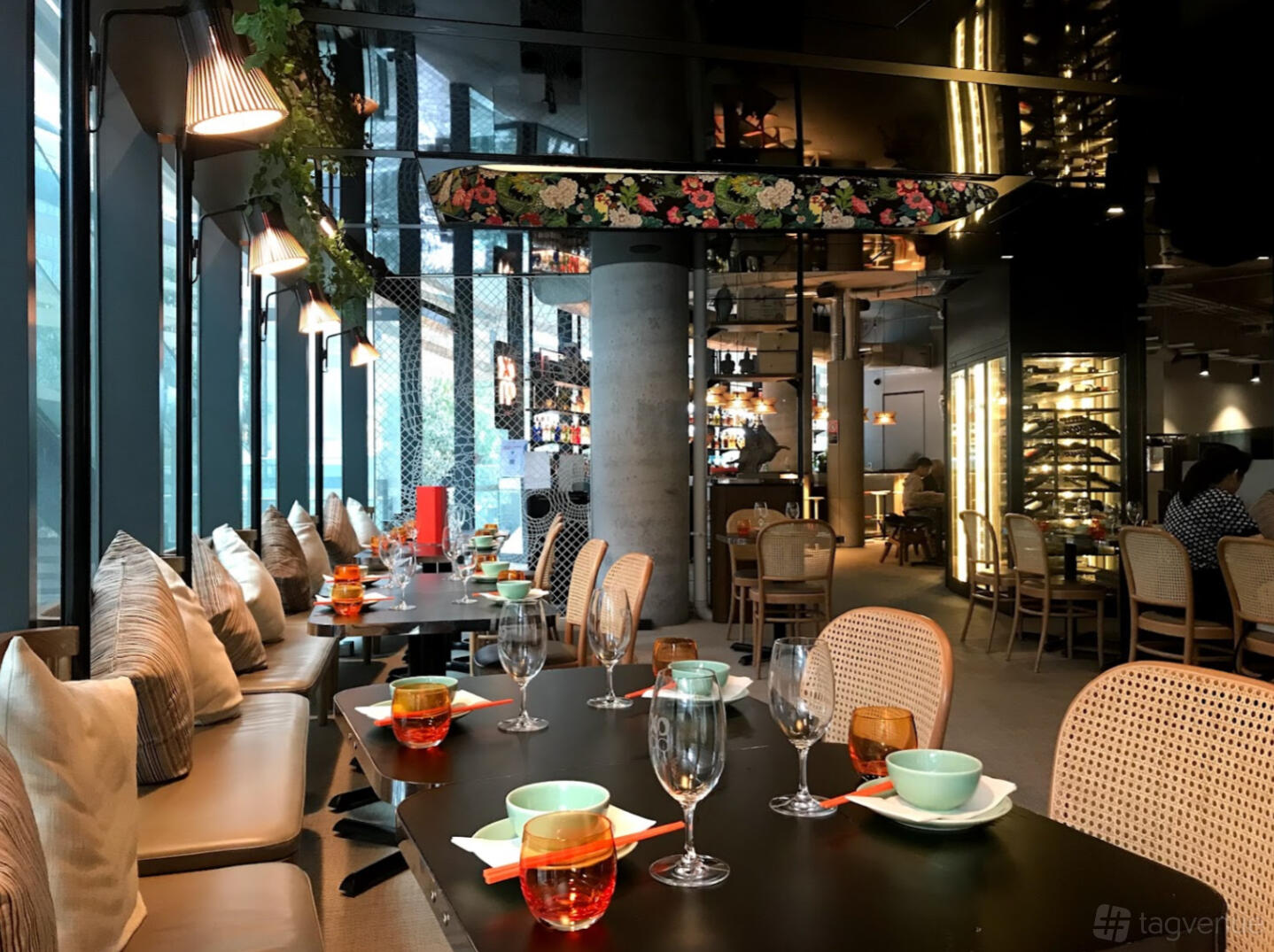 A restaurant with floor-to-ceiling windows, cushioned banquette seating, and tables set with glassware at XOPP.