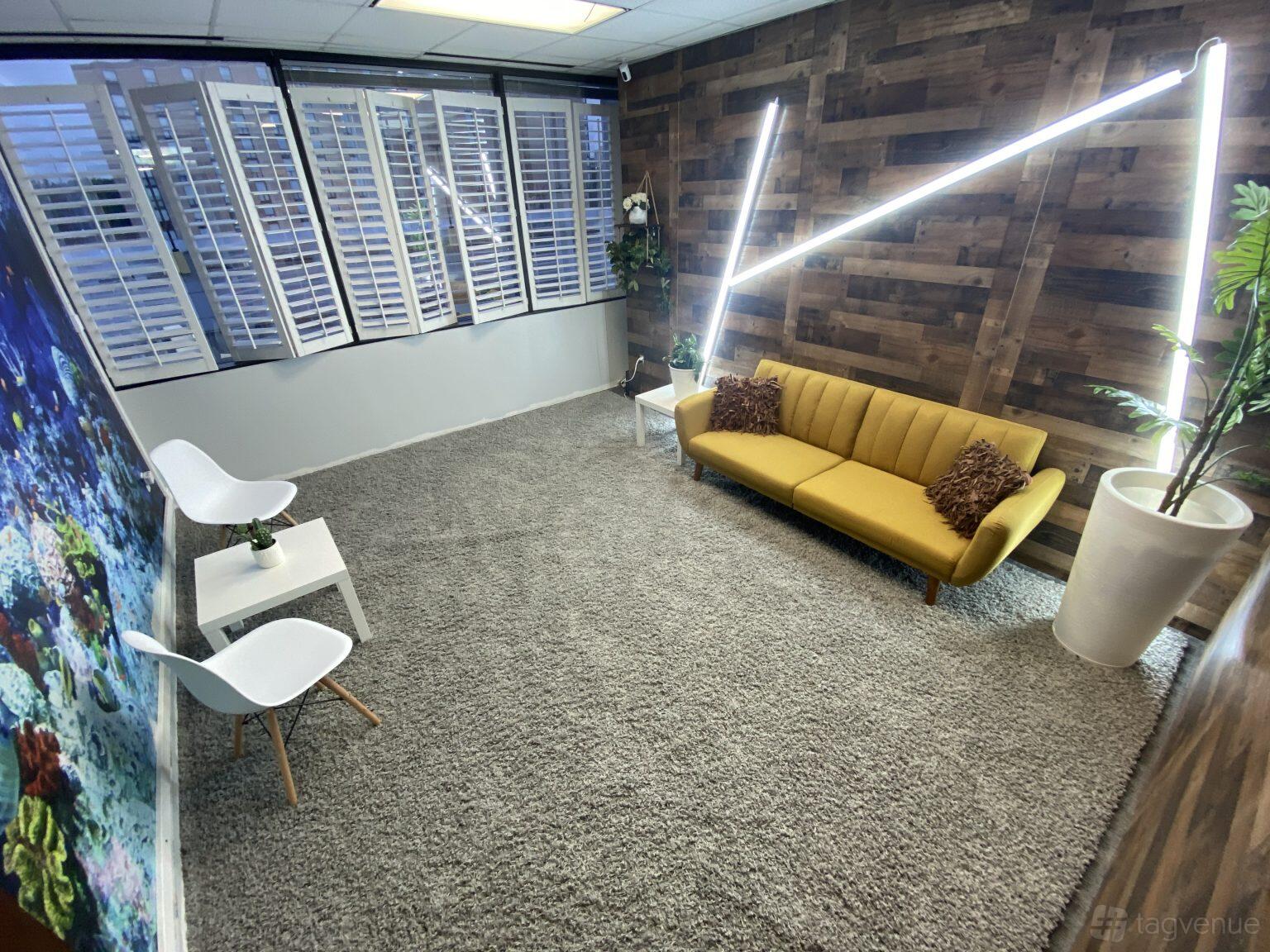 A photo studio with a yellow couch, wood accent wall, LED strip lighting, and large windows at North Houston Studio Space.