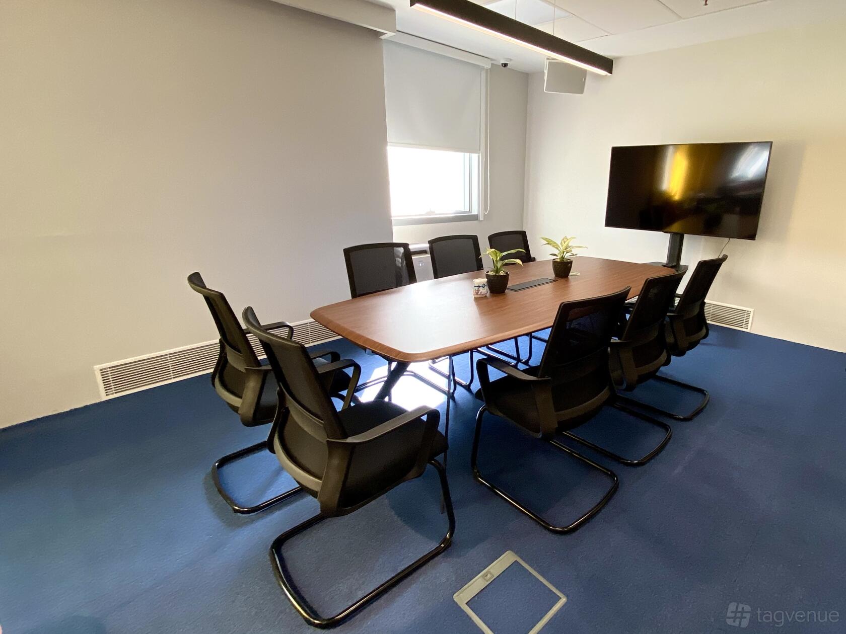 A meeting room with a rectangular wooden table, black chairs, potted plants, and a wall-mounted screen at Meeting Room (NTU Alumni Club Chill@5).
