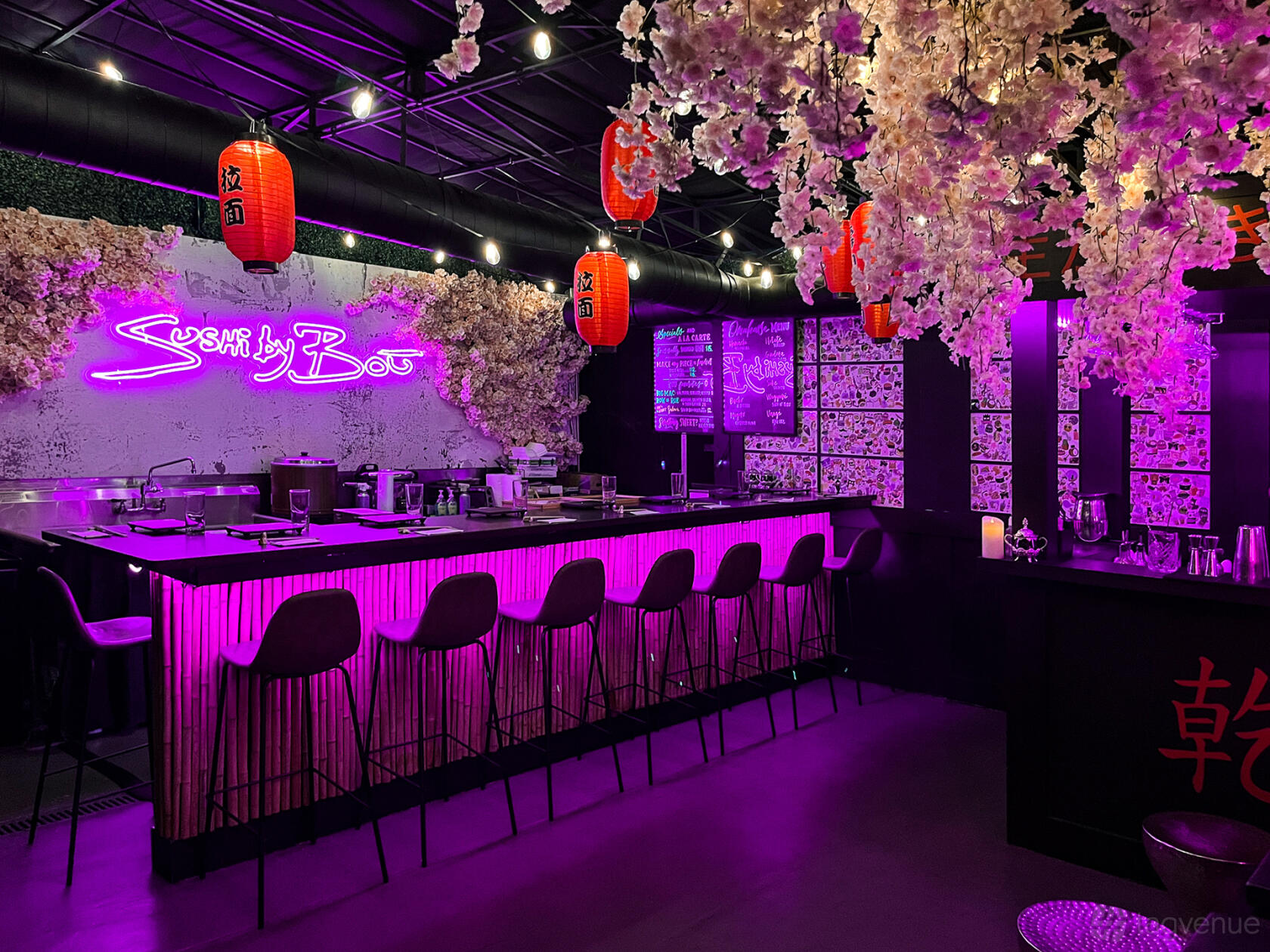 A restaurant with a sushi bar, pink neon lighting, cherry blossom decor, and red lanterns at Sushi by Bou Jersey City.