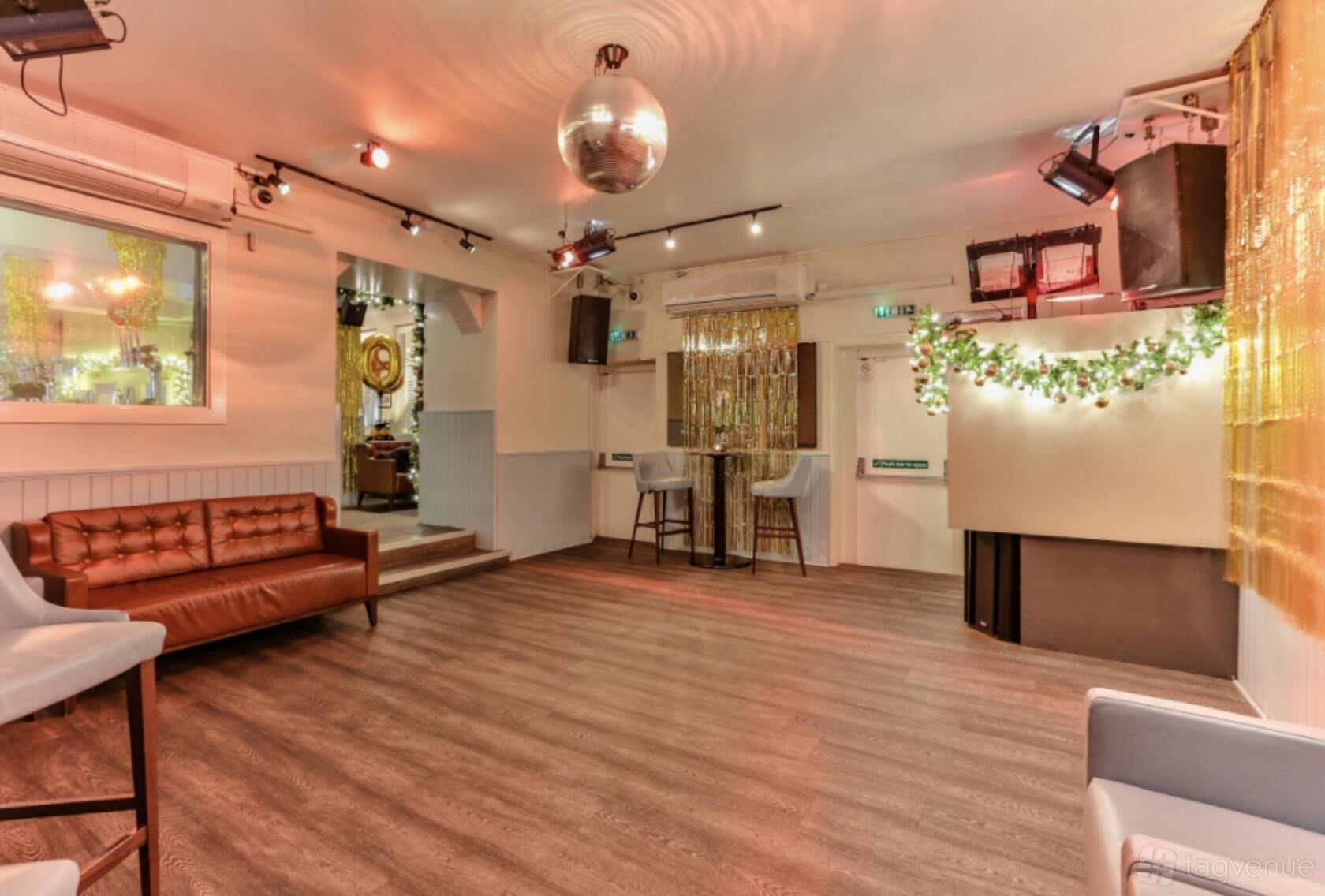 A function room with a disco ball, wood floors, brown leather sofas, and hanging greenery at The Chapel Bar.