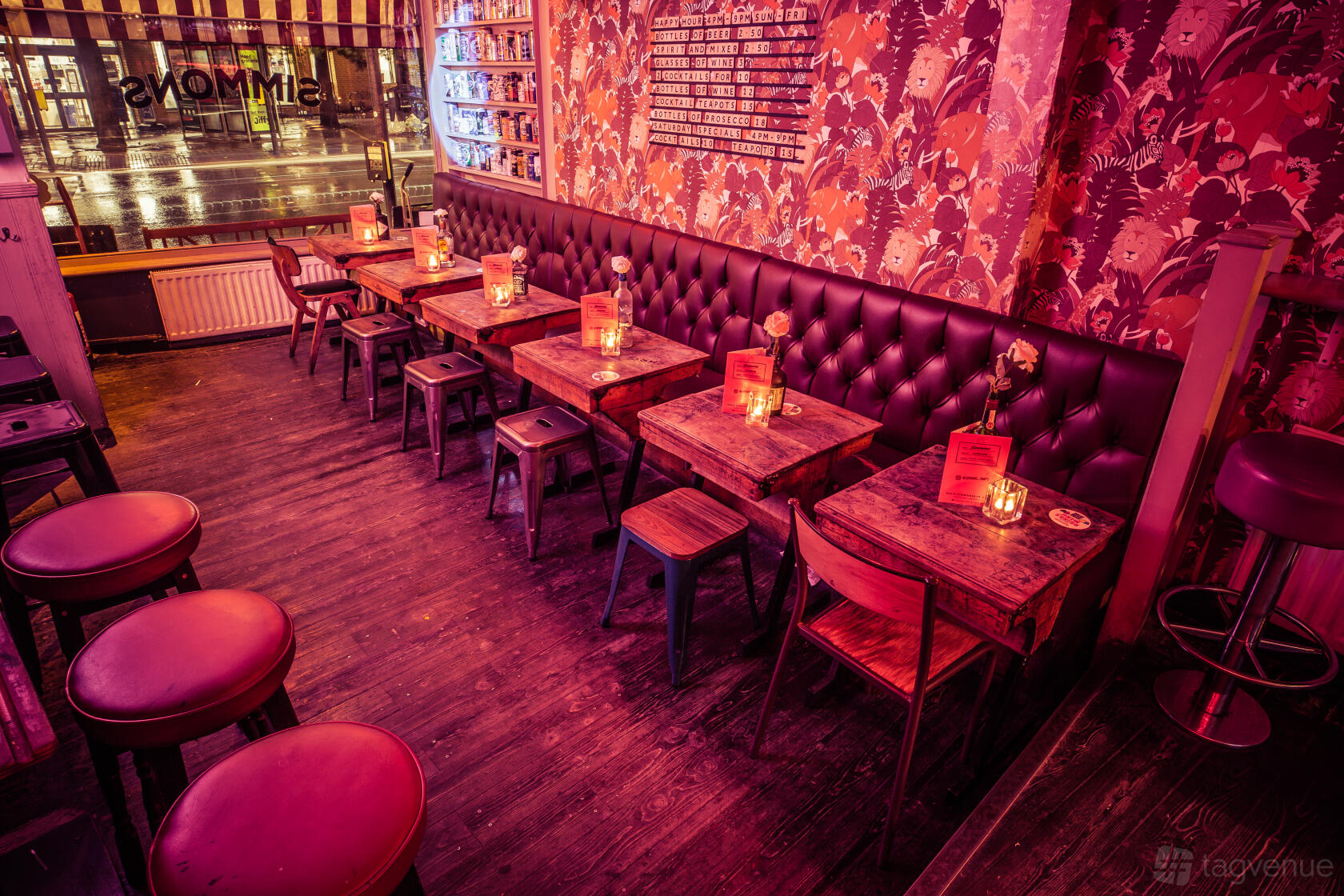 A cocktail bar with tufted leather banquette seating, patterned wallpaper, and candlelit wooden tables at Simmons | Kings Cross.