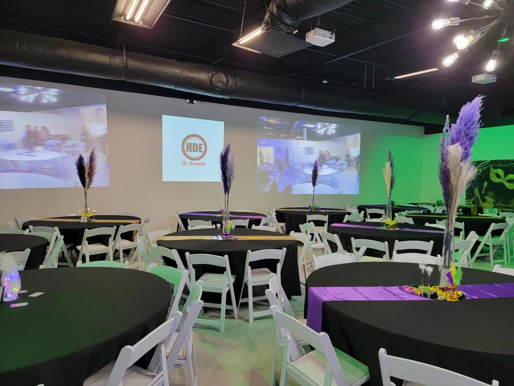 An event venue with round tables covered in black linens, white chairs, and tall centerpiece arrangements at Hi-Def Events of Avondale.