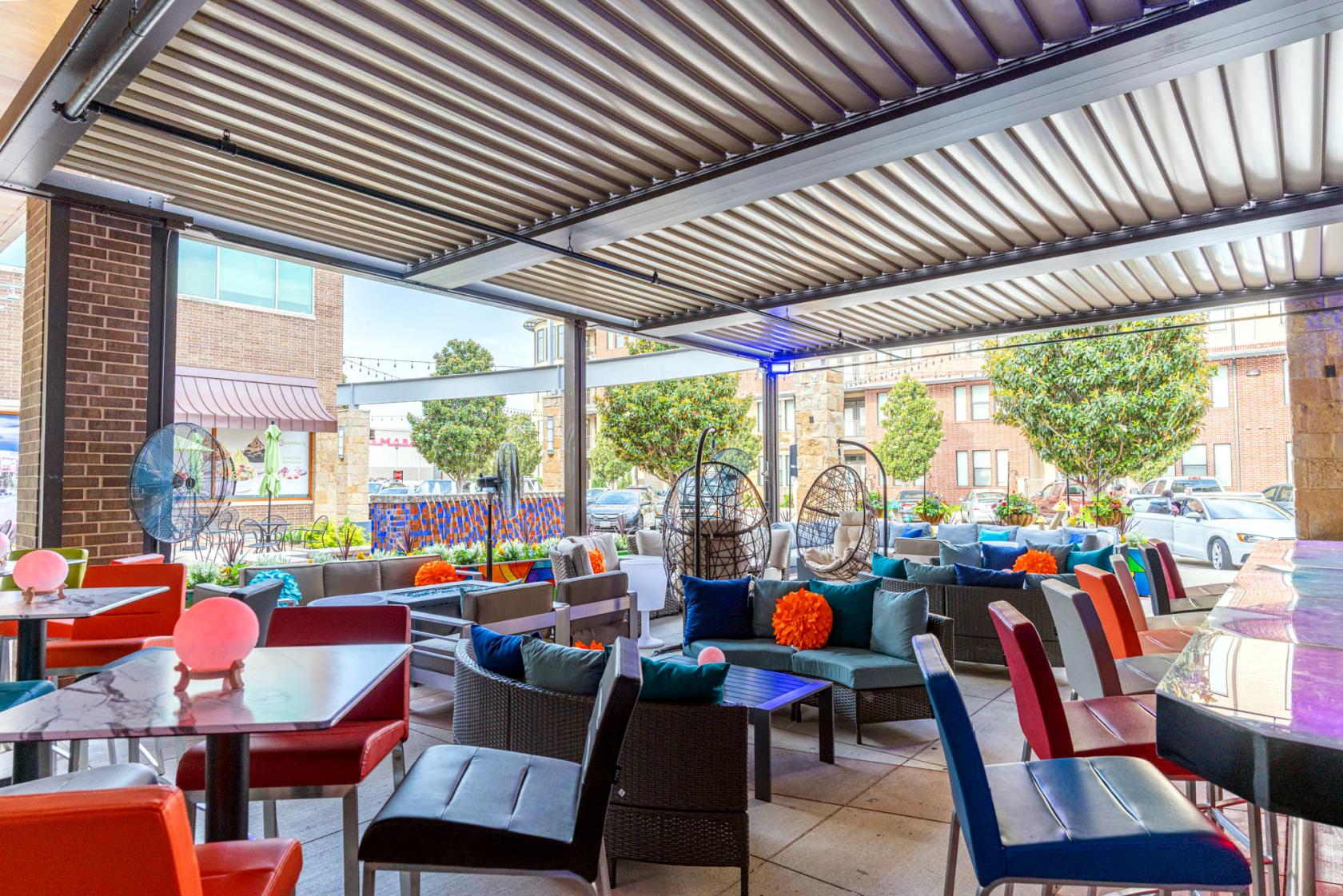 An outdoor patio with colorful chairs, cushioned lounge seating, and a louvered pergola at Fizz.