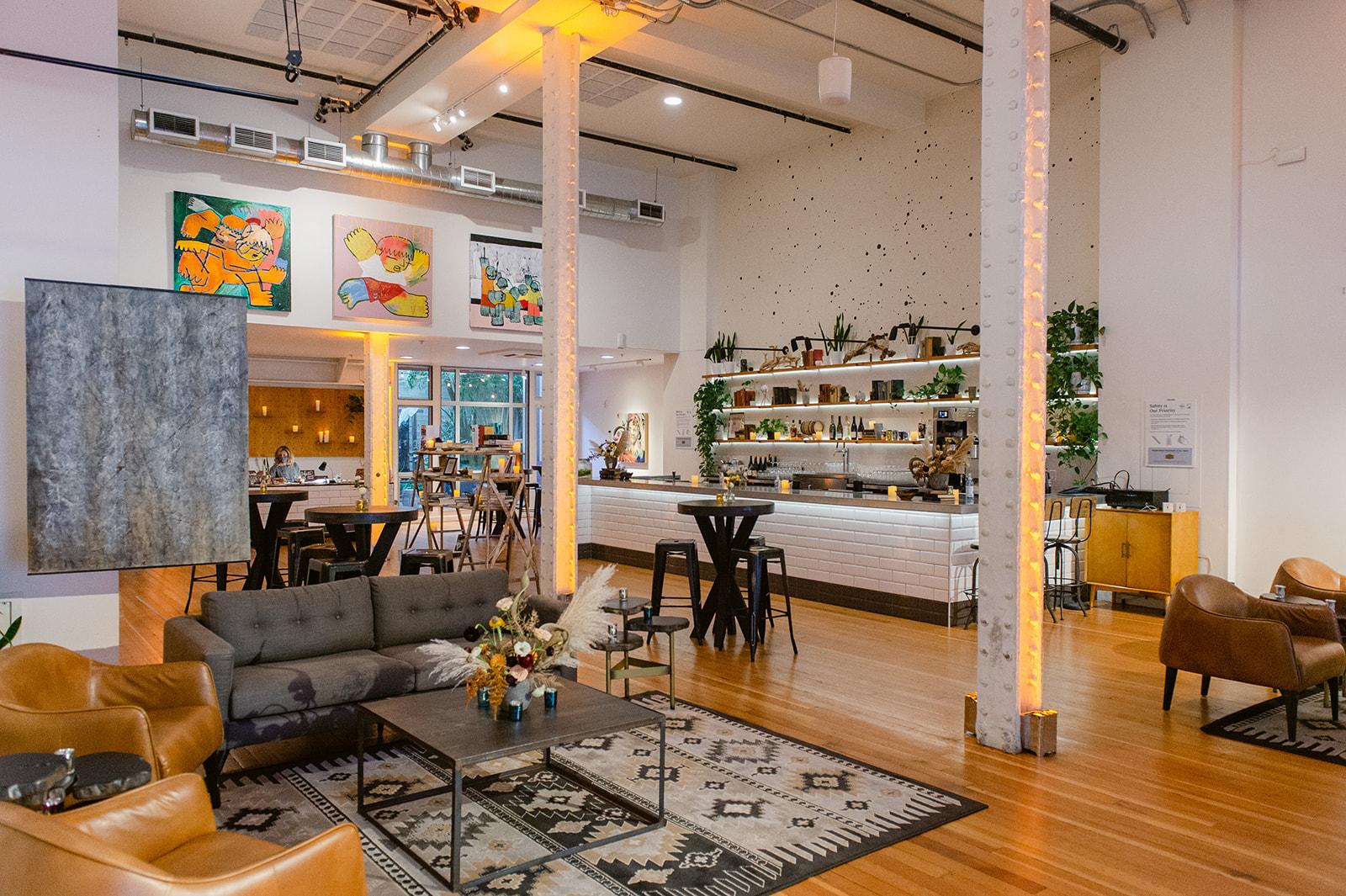 An event space in a bar with high ceilings, polished wood floors, wall art, and a long shelf-lined bar at The Alice Collective.