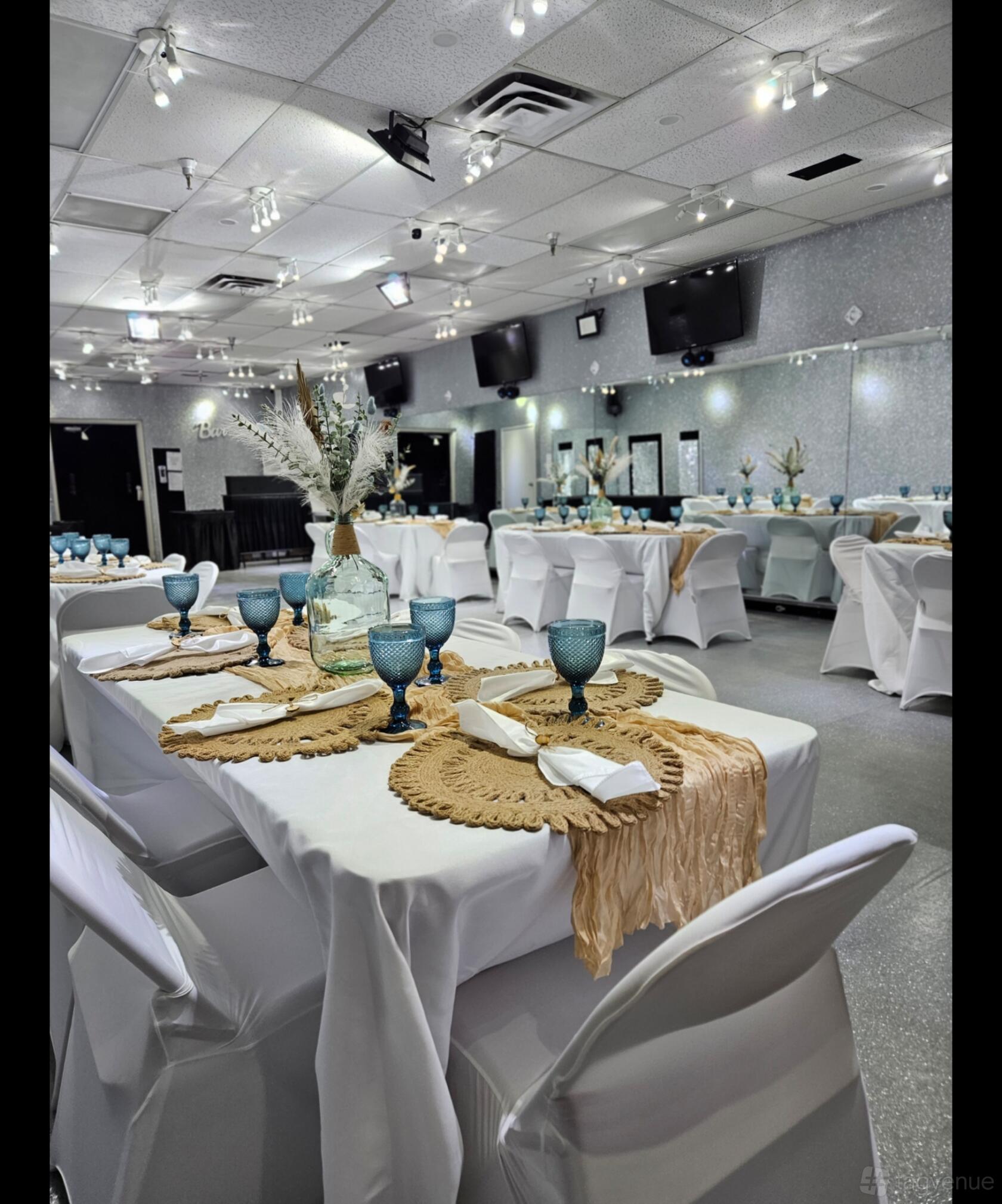 A function room with white-clothed rectangular tables, blue glassware, and mirrors along one wall at Icebox LV.