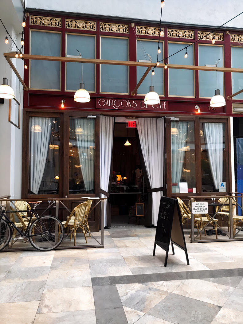 A pub with an outdoor patio featuring rattan chairs, small tables, and curtained glass doors at Garcons de Café.
