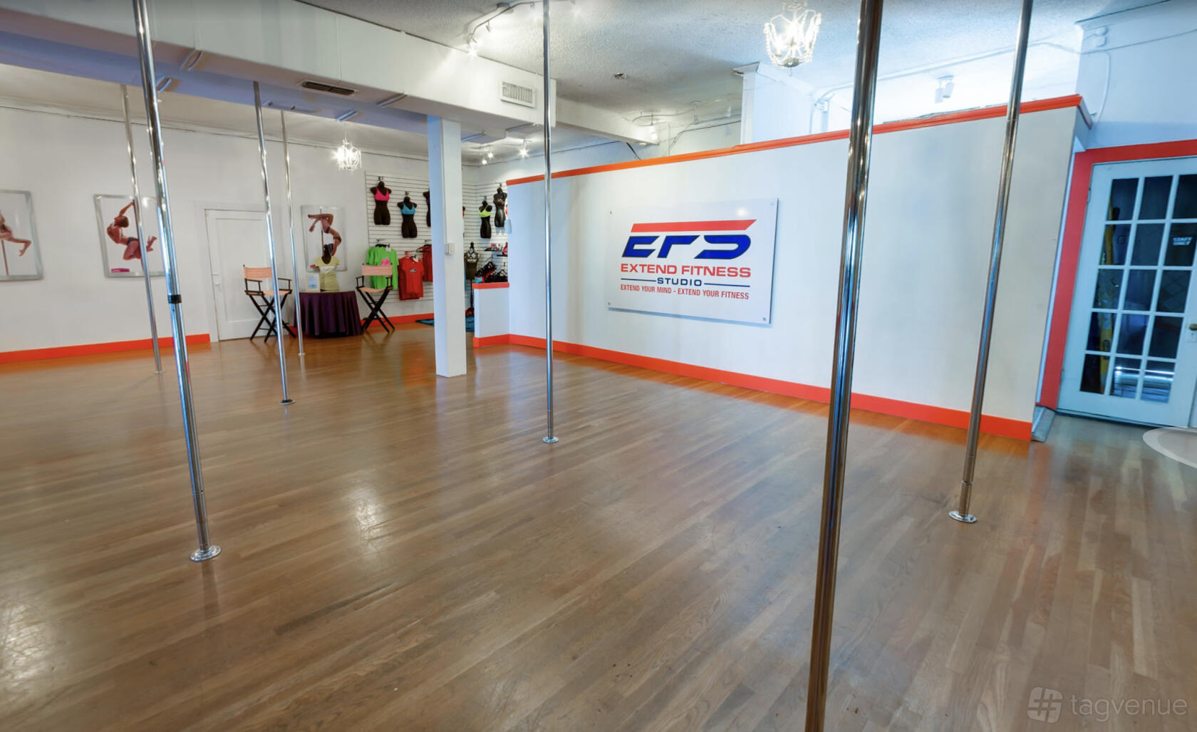 A dance studio with polished wooden floors, fitness poles, and wall mirrors at Extend Fitness Studio.