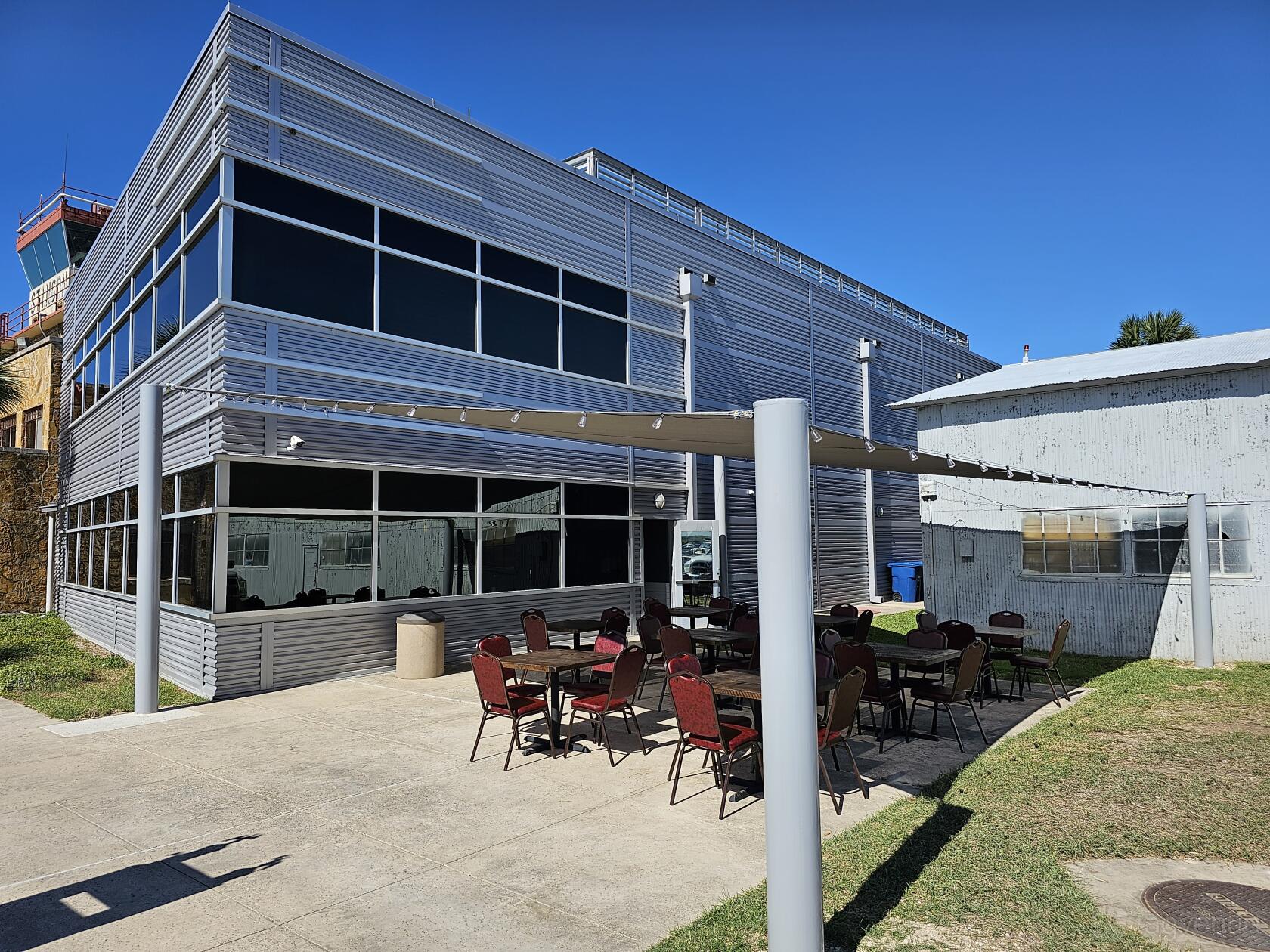 An outdoor restaurant patio with red cushioned chairs and round tables under a metal pergola at Trailblazer Café.