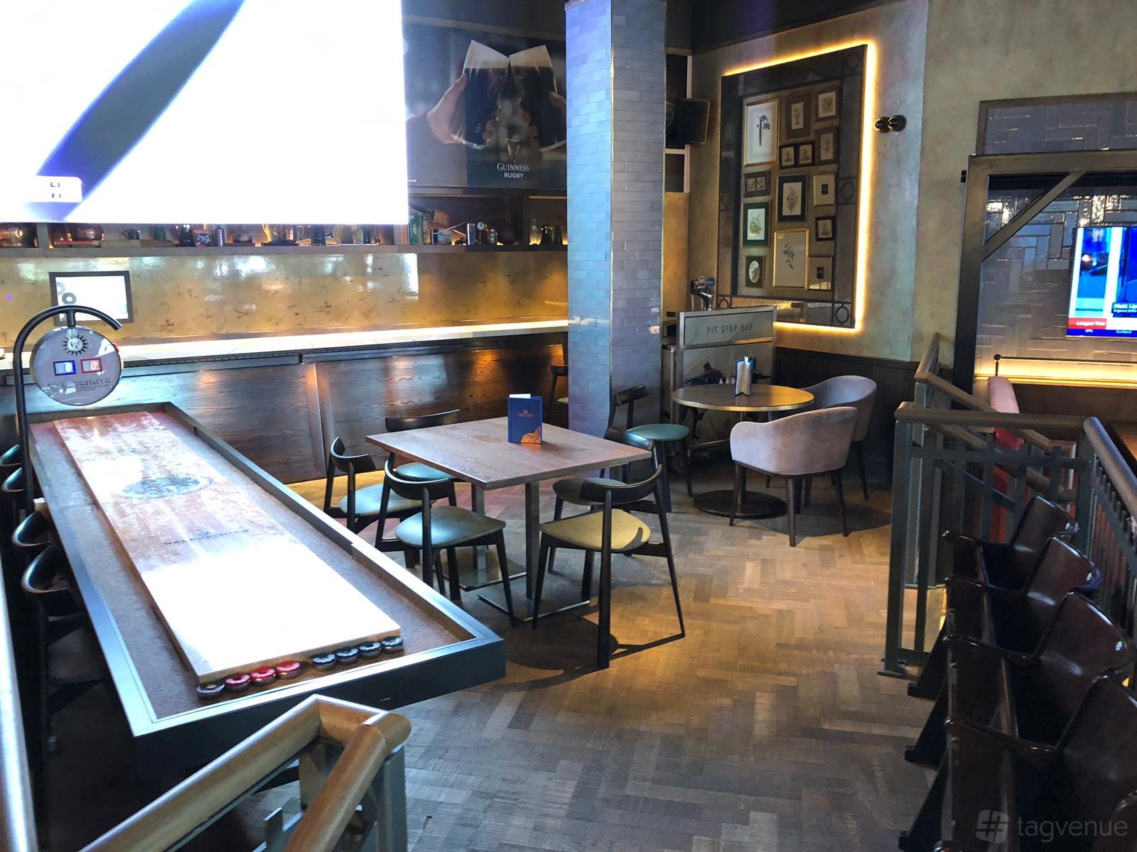A lounge in a bar with shuffleboard, wooden tables, and upholstered chairs at Westwood.