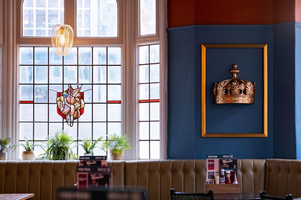 An event space in a pub with stained glass windows, tufted banquette seating, and a framed crown at The Royal.