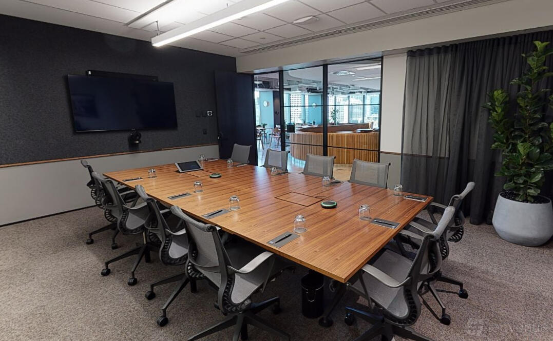 A coworking meeting room with a large wooden conference table, ergonomic chairs, and a wall-mounted screen at Hub Flinders Street.