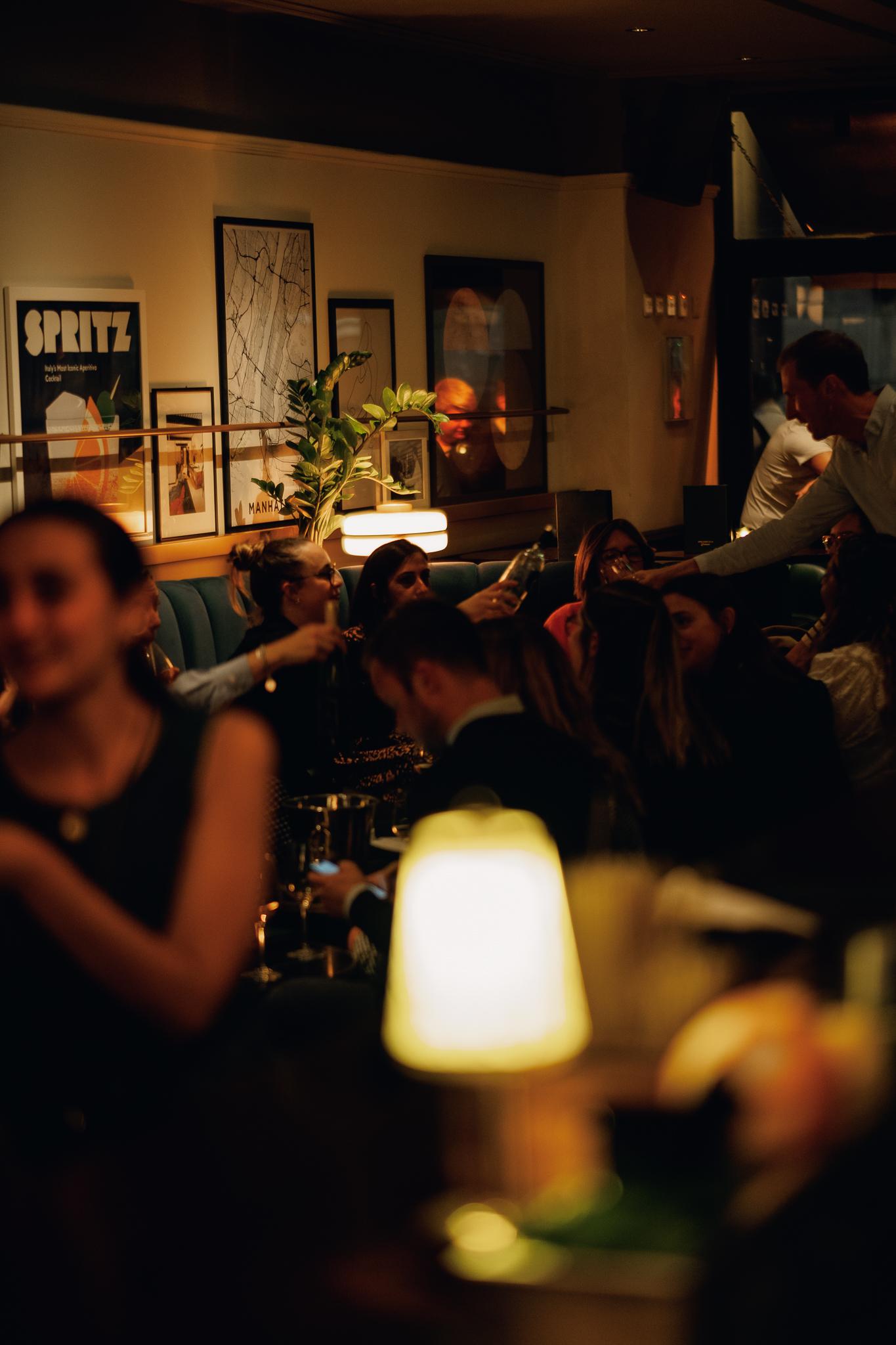 An underground cocktail bar with plush teal banquette seating, low lighting, and framed artwork at LOCKES Bar Covent Garden.