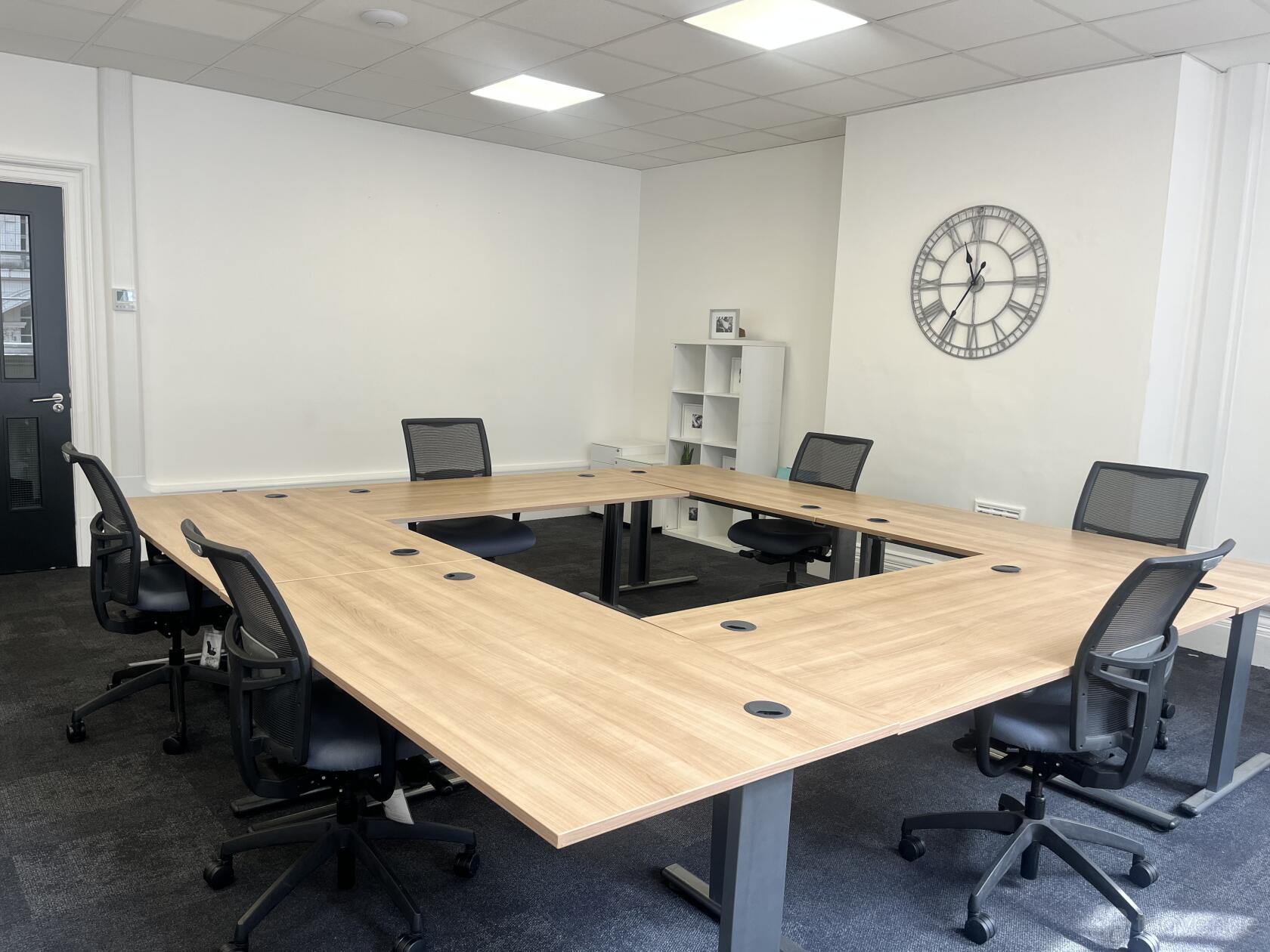 A boardroom with U-shaped wooden tables, mesh office chairs, and a wall clock at Airivo Birmingham.