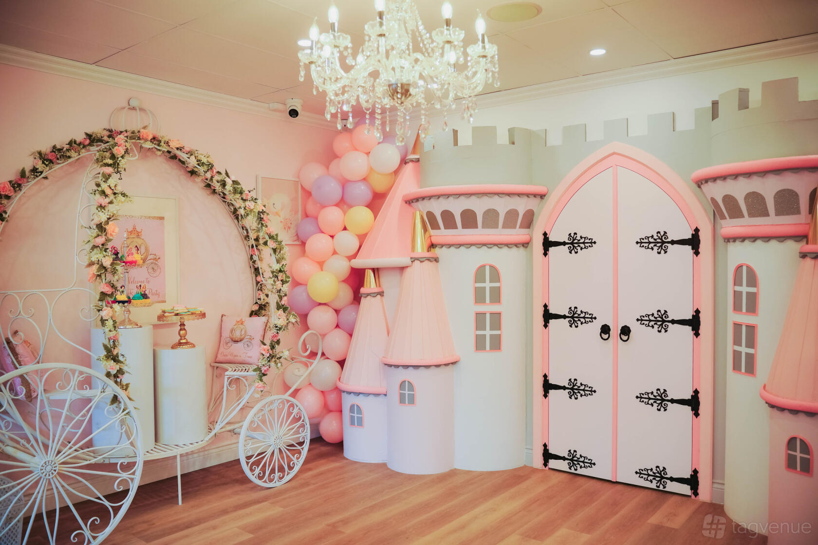 An event venue with a fairytale carriage, pink castle decor, pastel balloon display, and chandelier at My Royal Party.