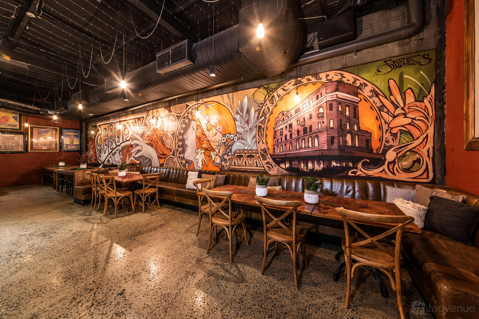 An event space in a bar with a long leather banquette, wooden tables, and mural-covered walls at Embassy Hotel.