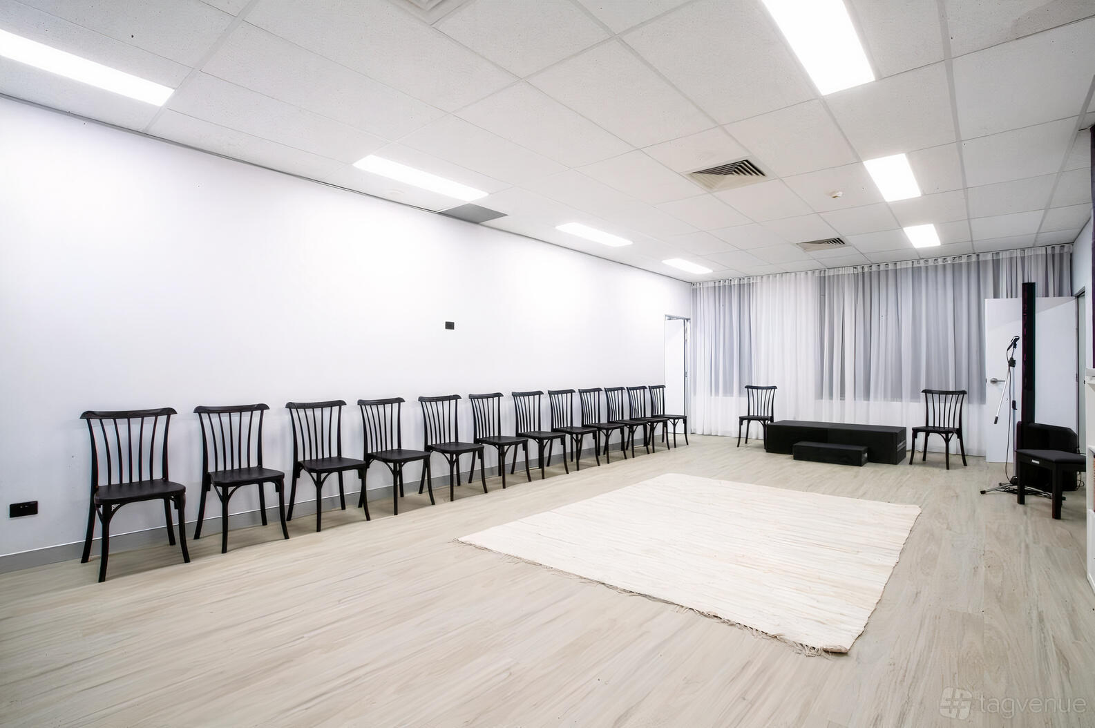 An event venue with a spacious studio, light wood floors, black chairs along the wall, and white curtains at Performance Studios Australia.