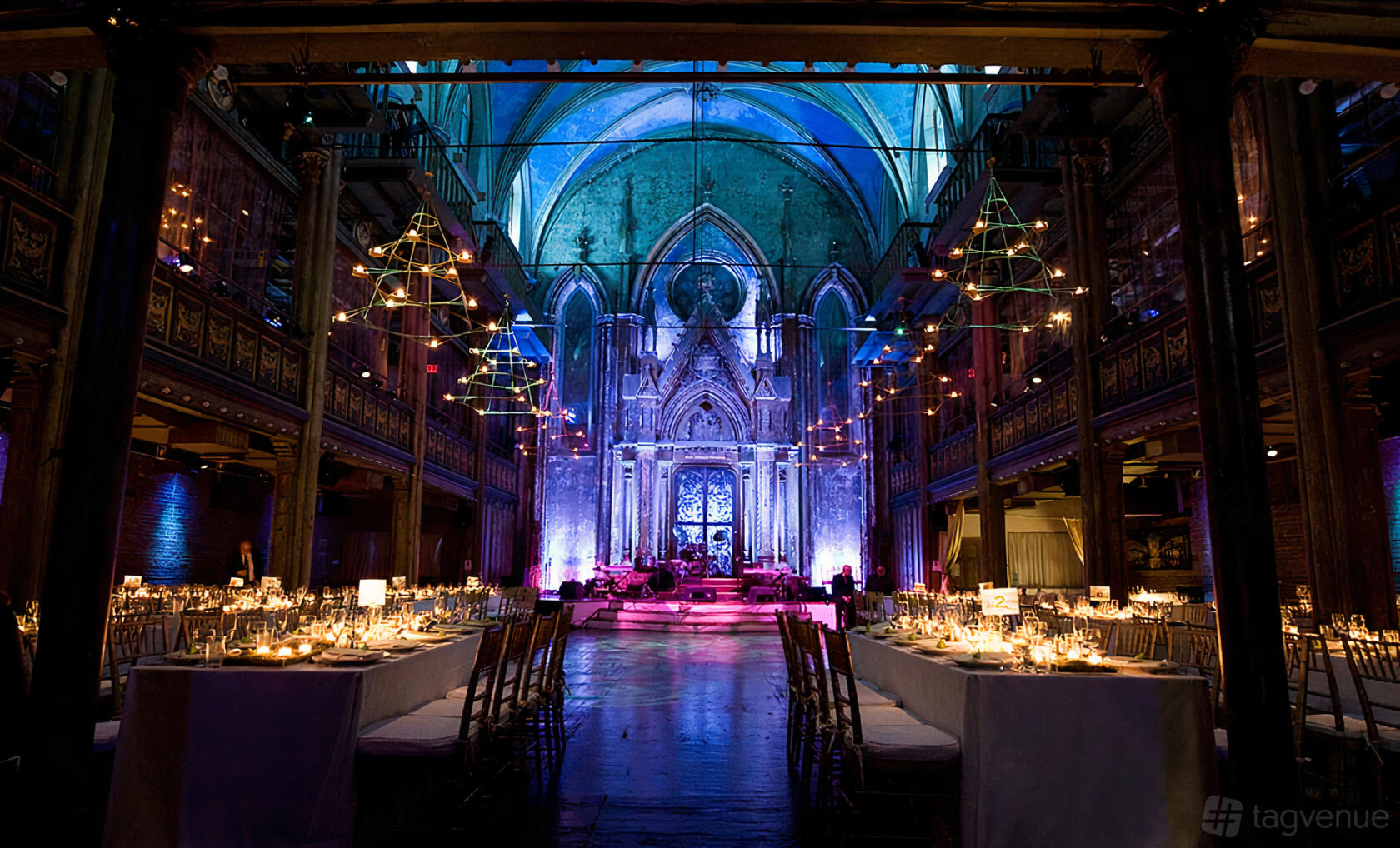 A historic building with vaulted ceilings, gothic arches, and long banquet tables with candles at Orensanz Events.