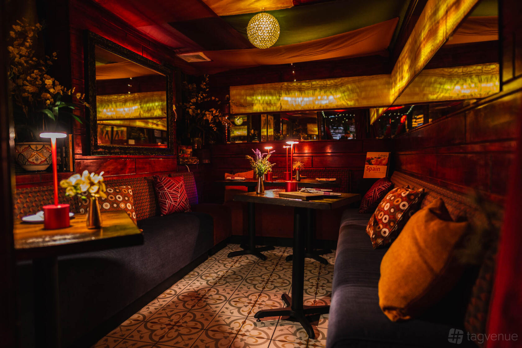 A restaurant with patterned tile floors, upholstered bench seating, warm lighting, and decorative cushions at Pil Pil.