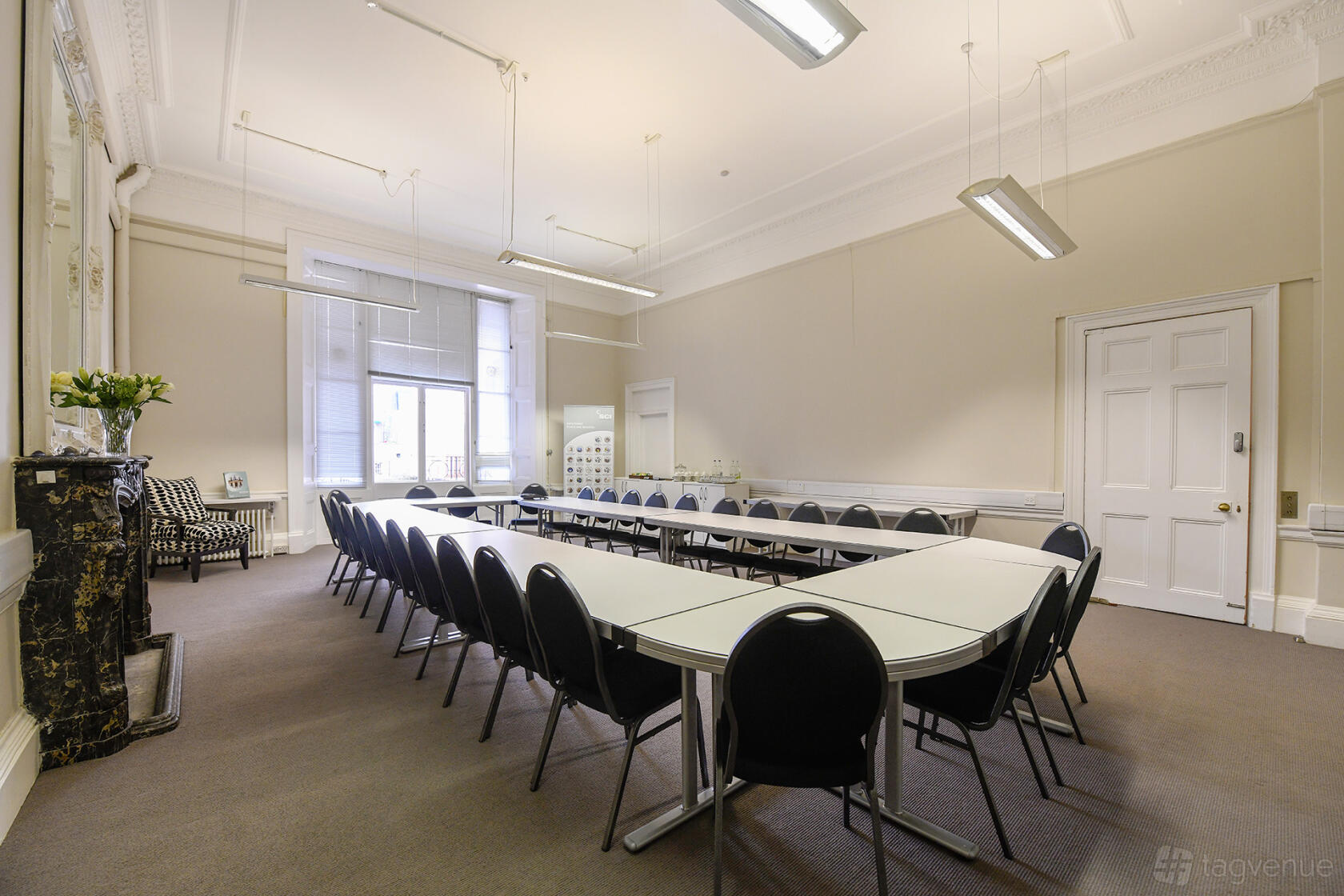 A meeting room with U-shaped tables, black chairs, large windows, and high ceilings at SCI Belgravia.