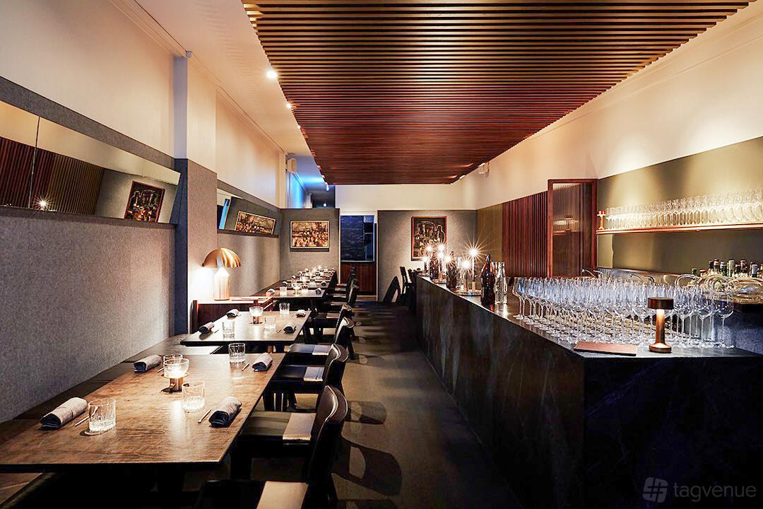 A bar in a restaurant with a polished stone counter, wooden ceiling slats, and rows of glassware at I D E S.