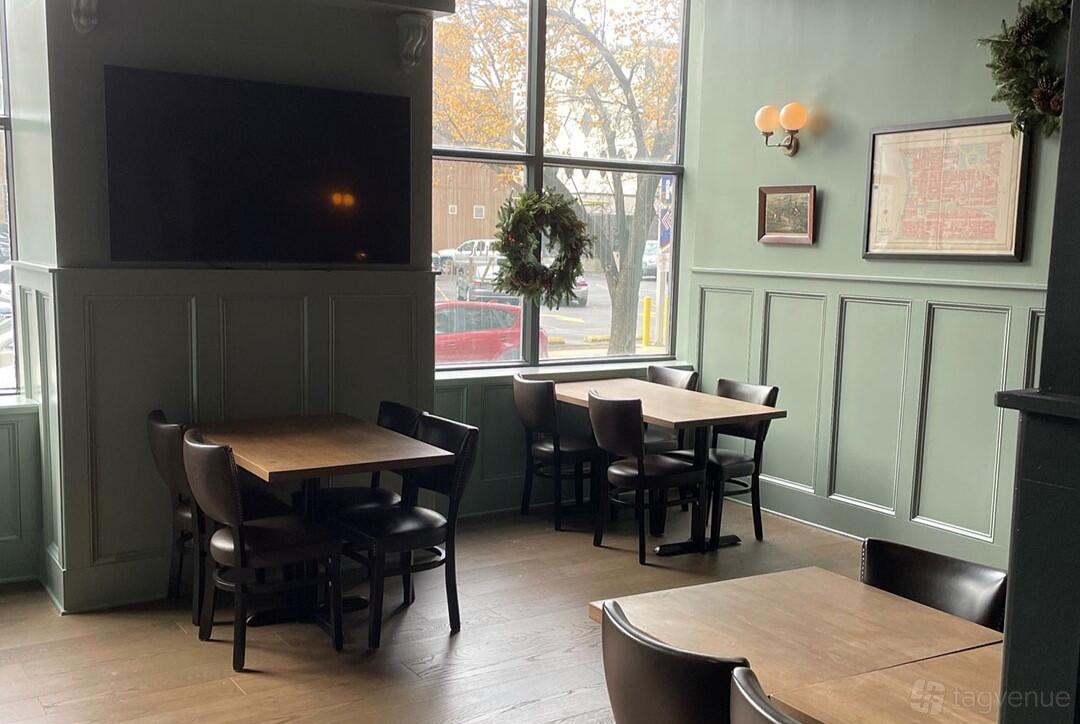 A lounge with large windows, wooden tables, black chairs, and soft wall lighting at The Mulberry.
