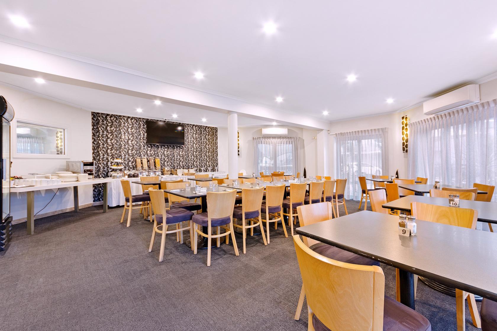 A hotel restaurant with wooden chairs, square tables, and floor-to-ceiling windows at Quality Resort Sorrento Beach.