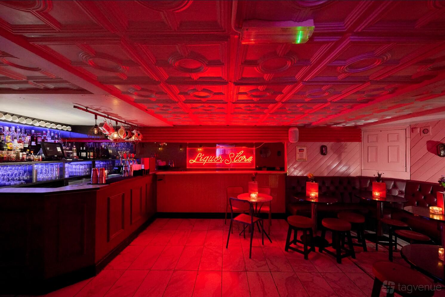 A function room in a cocktail bar with a neon sign, tufted banquette seating, and small candlelit tables at Simmons | Liverpool Street.